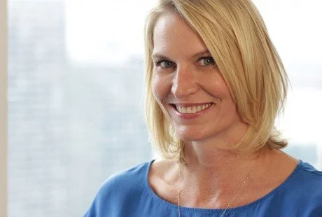 Josette Persson is three-time Emmy award-winning producer with an emphasis in storytelling, series producing, & show running for live television. A smiling woman with blonde hair wearing a blue top, standing in front of a blurred window background.