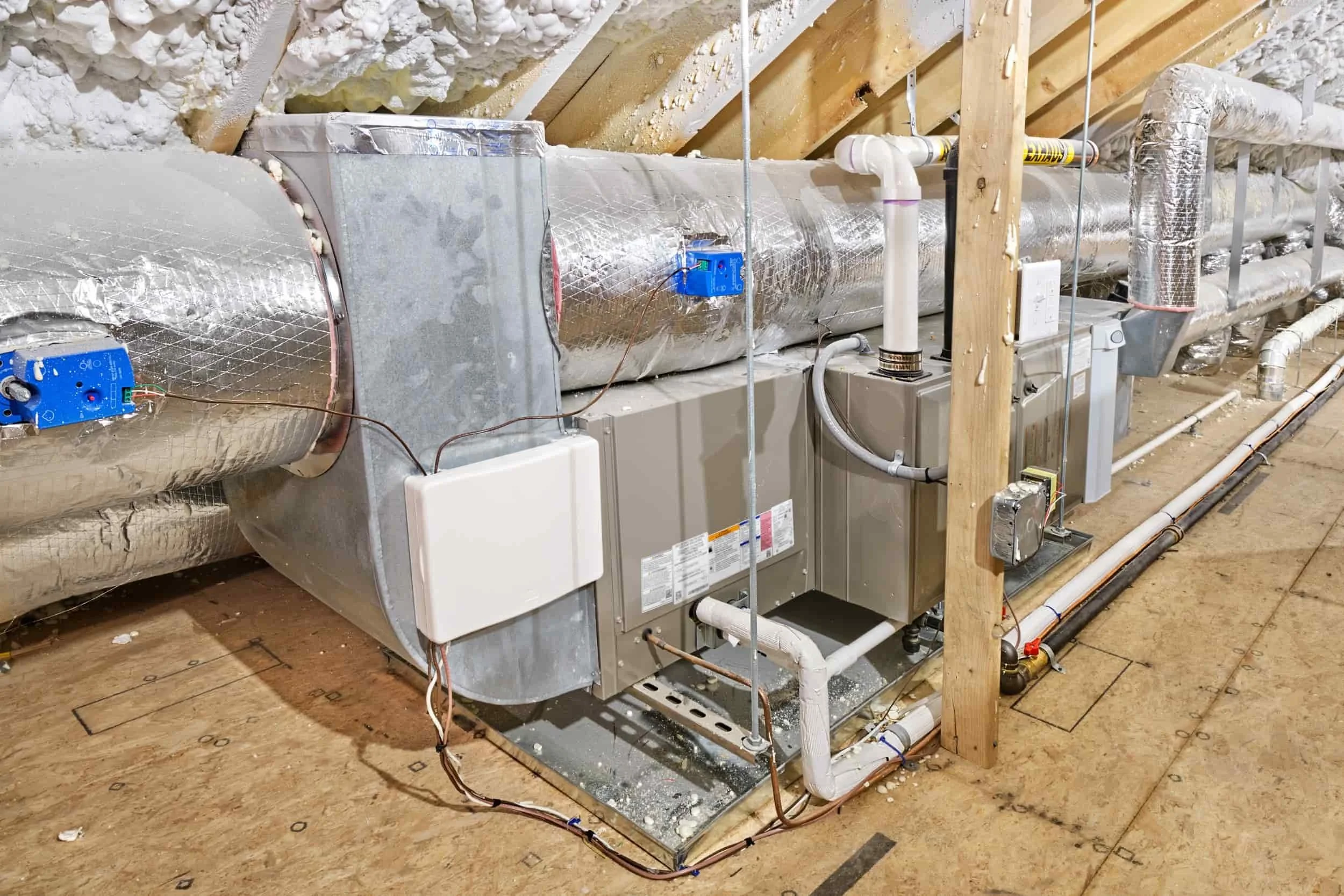 HVAC system unit with insulated ducts and wiring installed in an unfinished attic with spray foam insulation on the roof.