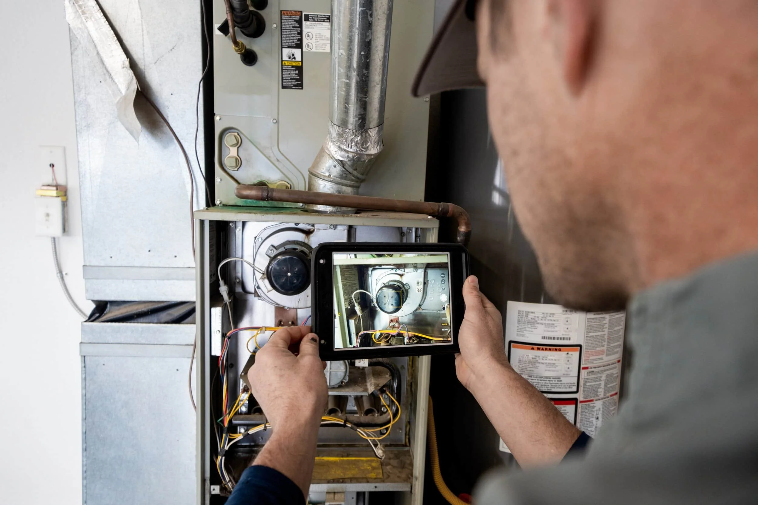 Person taking a photo of an open furnace unit with a tablet, inspecting or repairing its internal components.