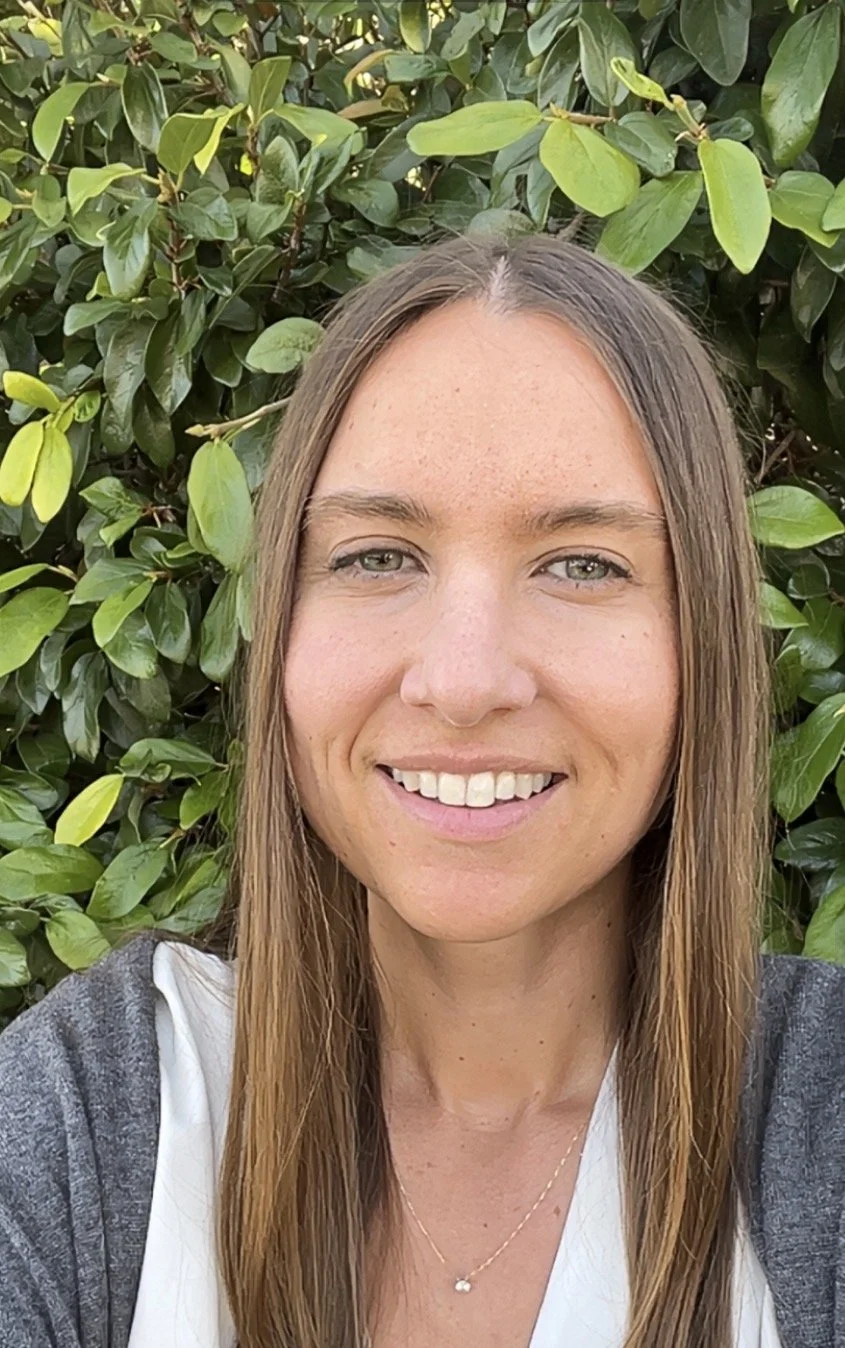 Dr. Alexandra Lyon standing in front of green leafy bushes.