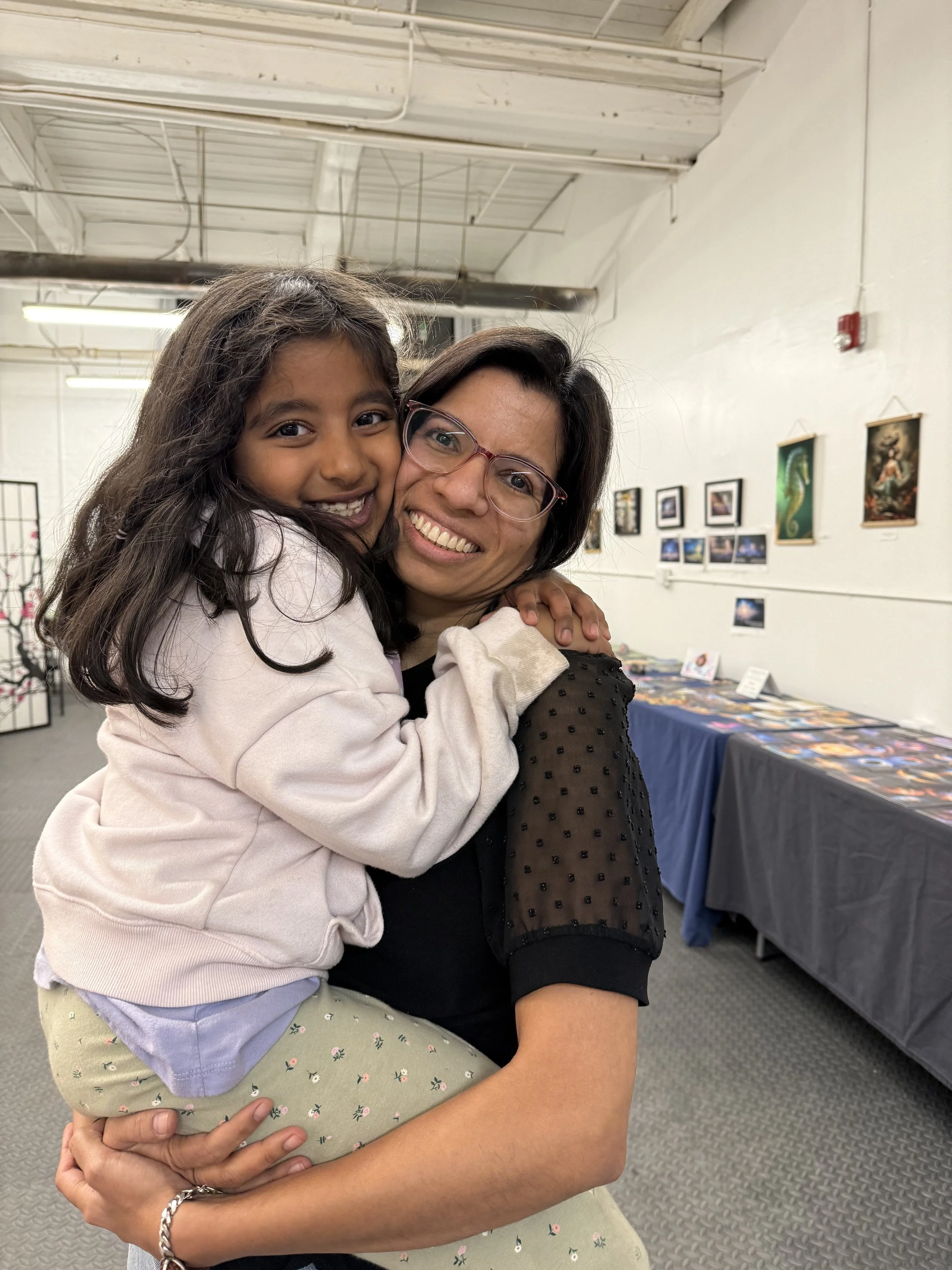 A woman and a young girl hugging and smiling in an art gallery.