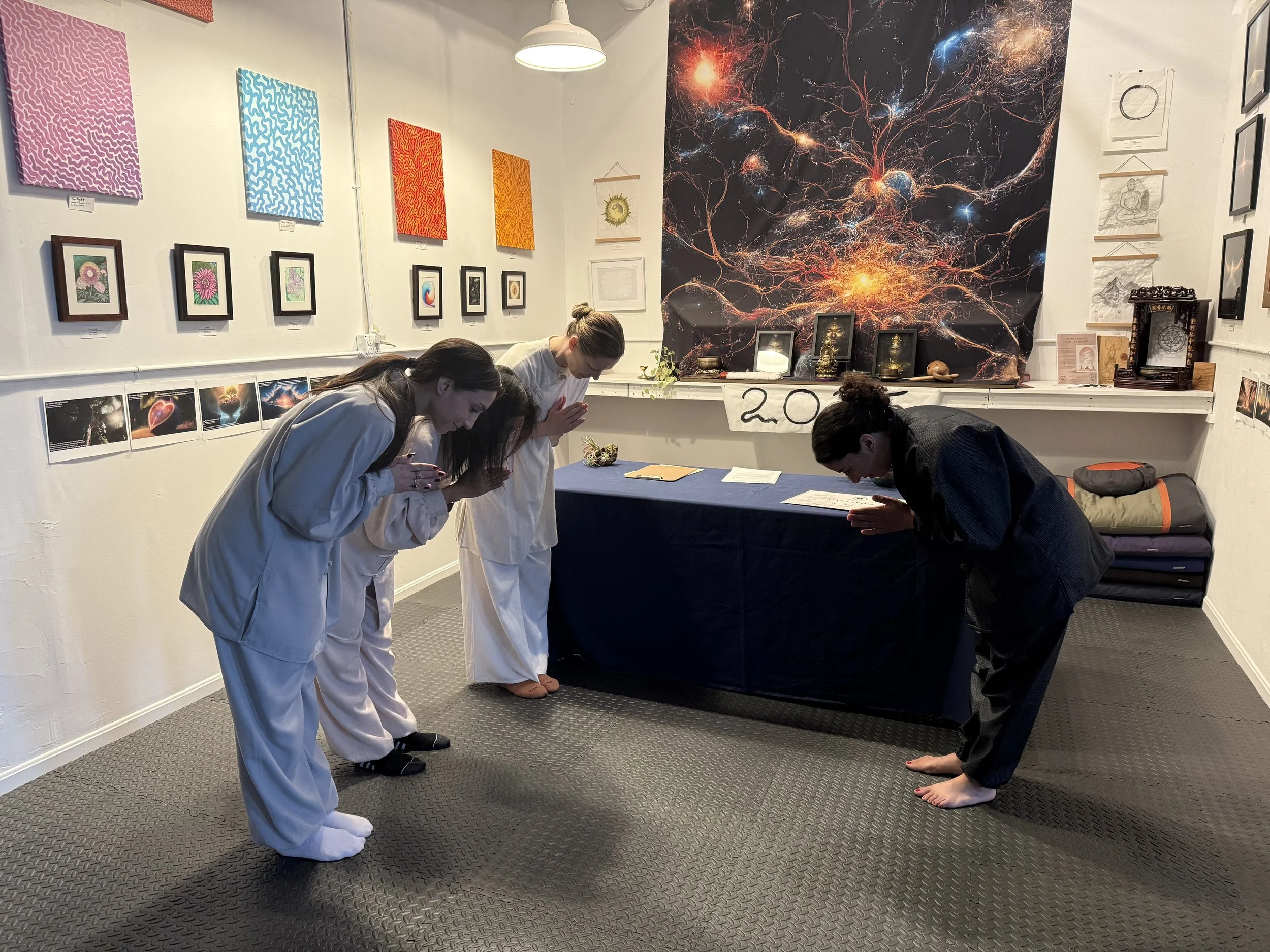 Three women and one man practicing a yoga or meditation pose in an art gallery.