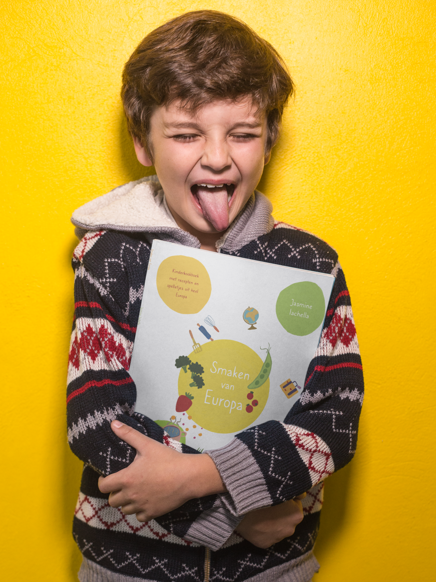 boy-sticking-his-tongue-out-holding-a-book-mockup-against-a-yellow-wall-a19217.png