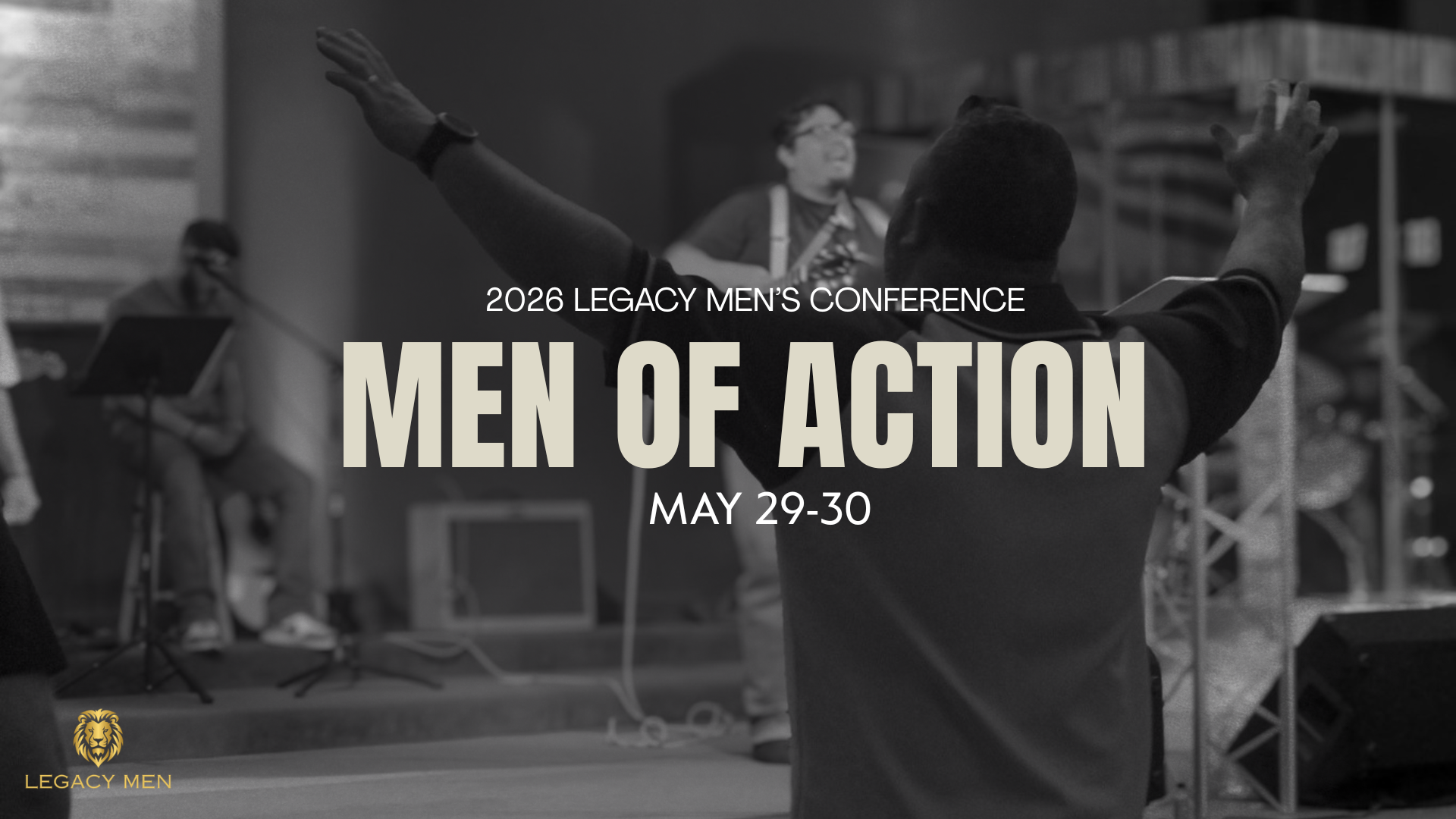 Black and white photo of a man with arms raised during a conference, with a woman speaking at a desk in the background. Text overlay: "2026 Legacy Men’s Conference Men of Action May 29-30", logo of a lion's head with the words "Legacy Men" at the bottom left.