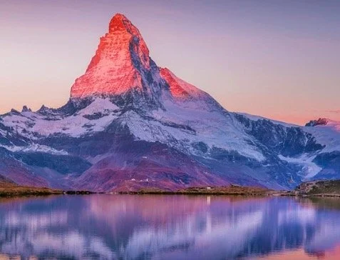 Mountain peak lit by sunrise with reflection in a lake.