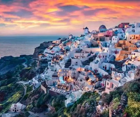 Sunset over the whitewashed buildings of Oia, Santorini, Greece, with a view of the Aegean Sea.