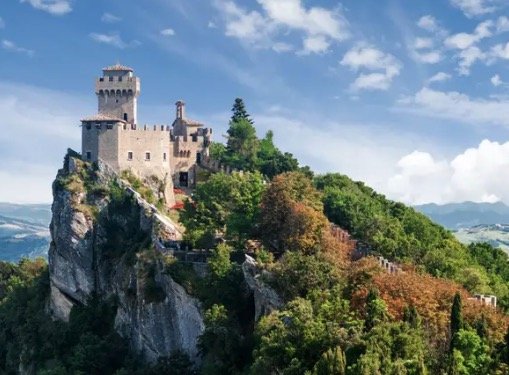 Castle on a hilltop surrounded by lush greenery under a blue sky