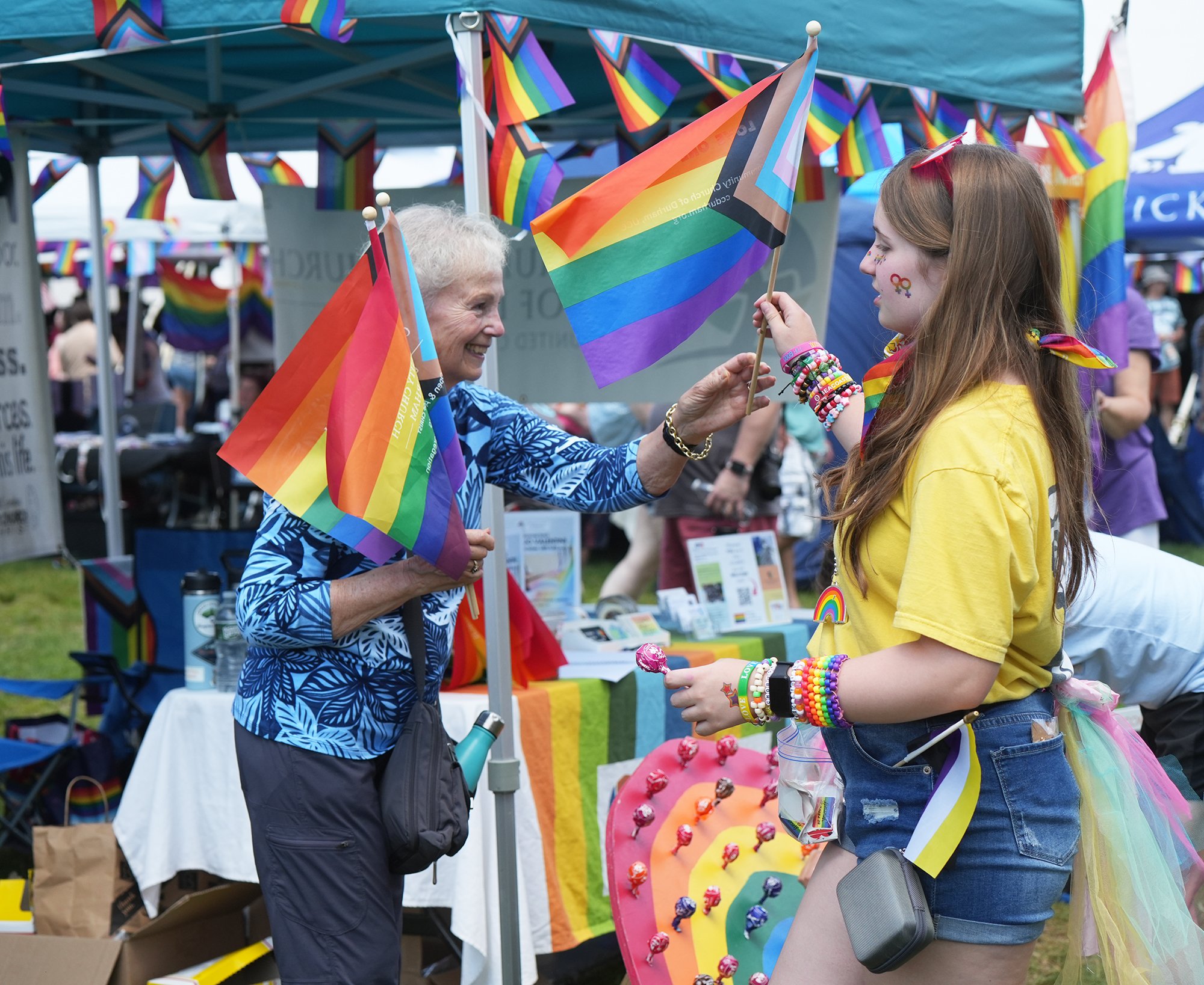 An older woman hands a progress Pride flag to a younger woman.