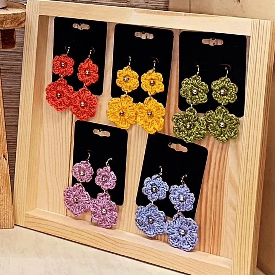Colorful crochet flower earrings displayed on black cards inside a wooden display frame.