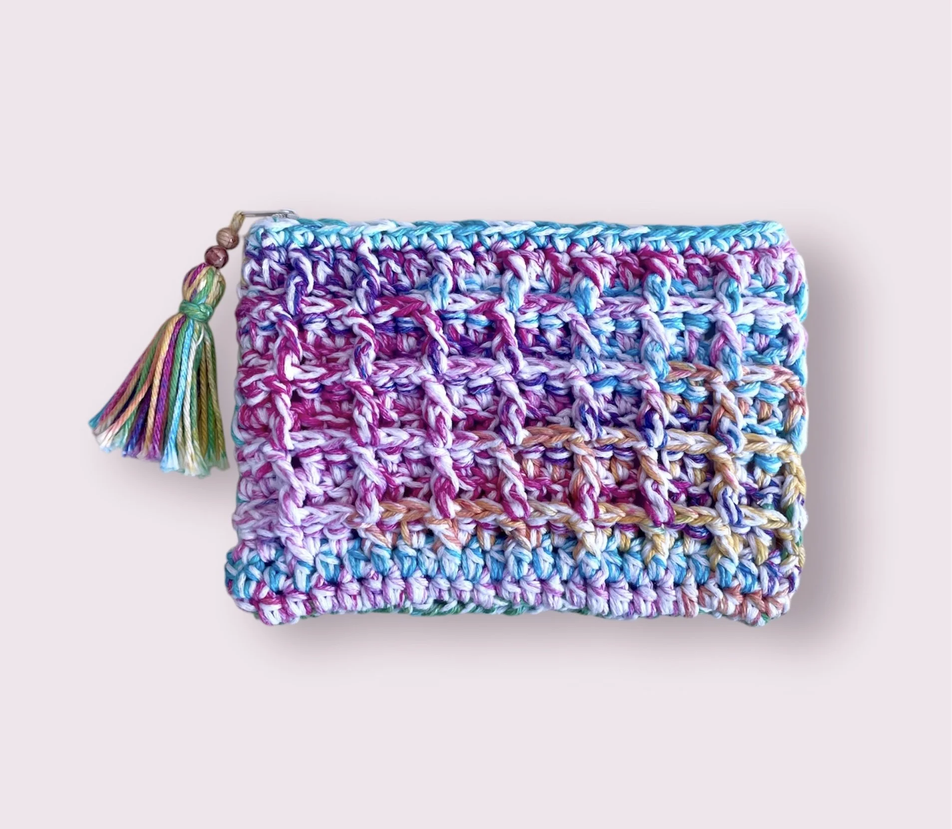Close-up of a multicolored, crocheted knit clutch with a rainbow tassel on the side, placed against a plain, light background.