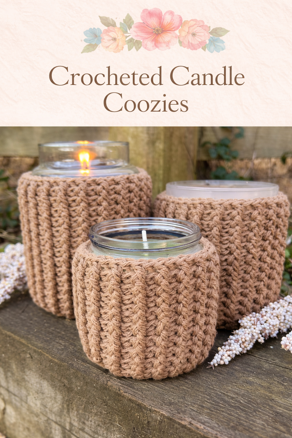 Three candles in glass containers wrapped with crocheted covers, sitting on a wooden surface outdoors, with small white flowers nearby.