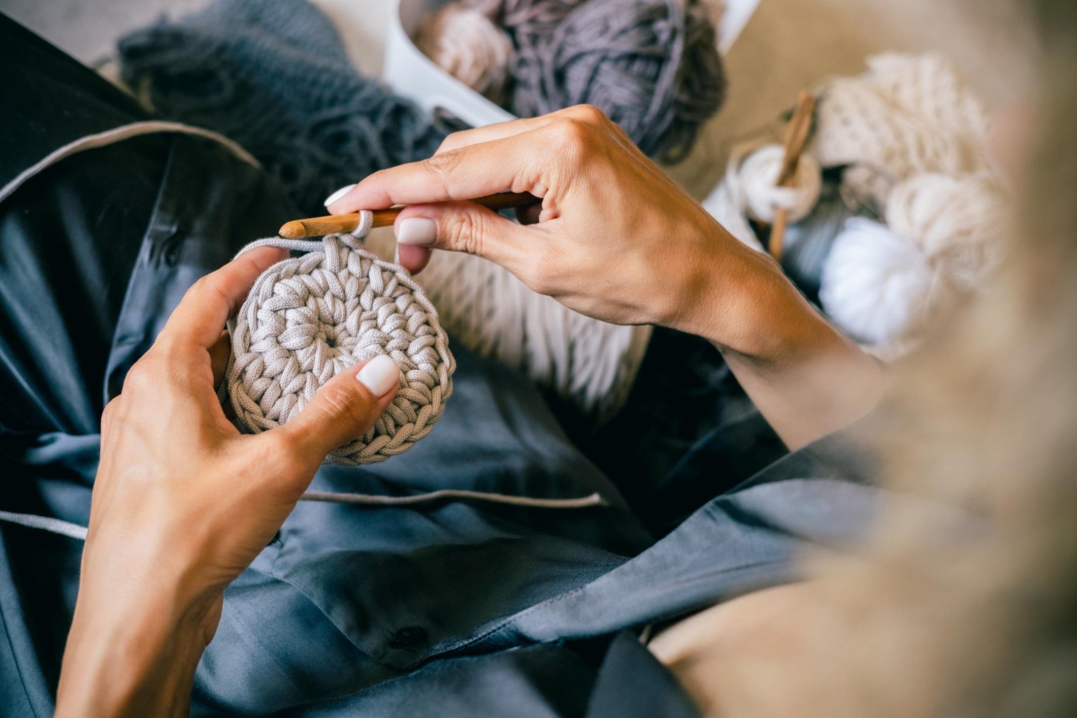 Person knitting beige yarn with wooden knitting needles, sitting on lap, with yarn balls in background.