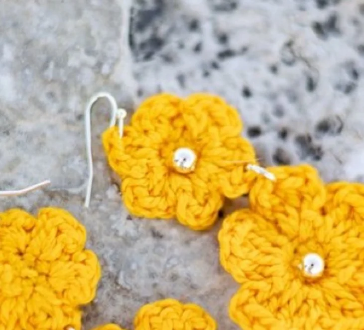 Yellow crocheted flowers with white beads in the center placed on a gray stone surface.