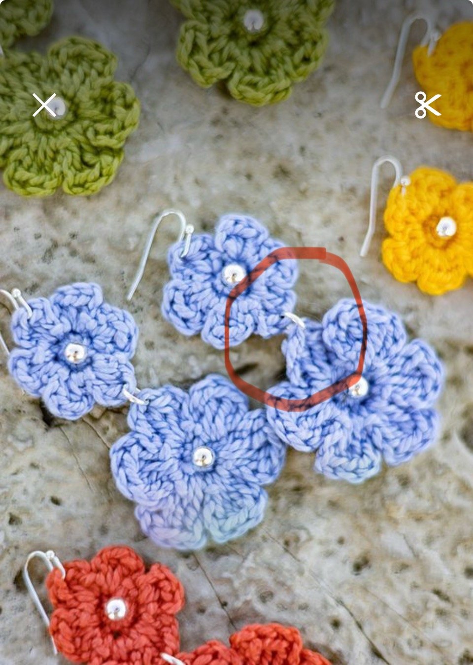 Colorful crochet flower earrings in green, yellow, blue, and orange, displayed on a marble surface.