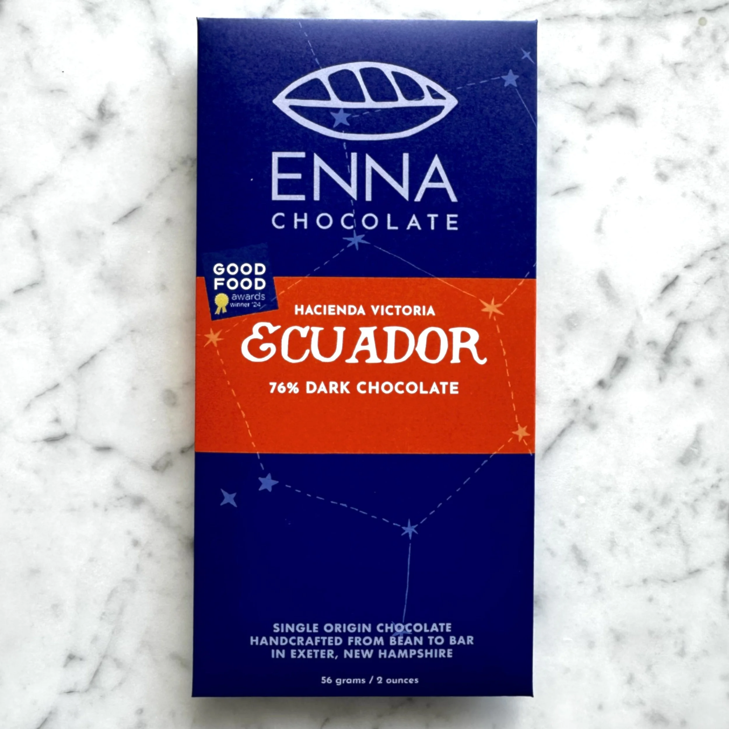 Blue packaging of Enna Chocolate with a white leaf logo, stars, and text indicating it is single origin, handcrafted from bean to bar in Exeter, New Hampshire, containing 56 grams or 2 ounces of dark chocolate.