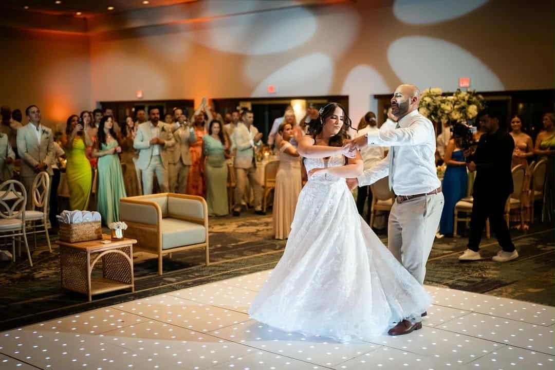 A bride and groom dancing on a lit-up dance floor at their wedding reception, with guests watching in the background.