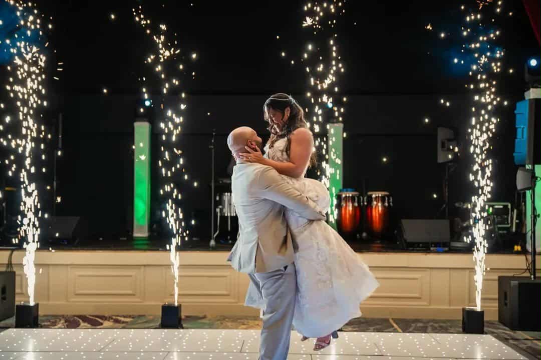 A couple dancing at a wedding reception with sparks and fireworks in the background.