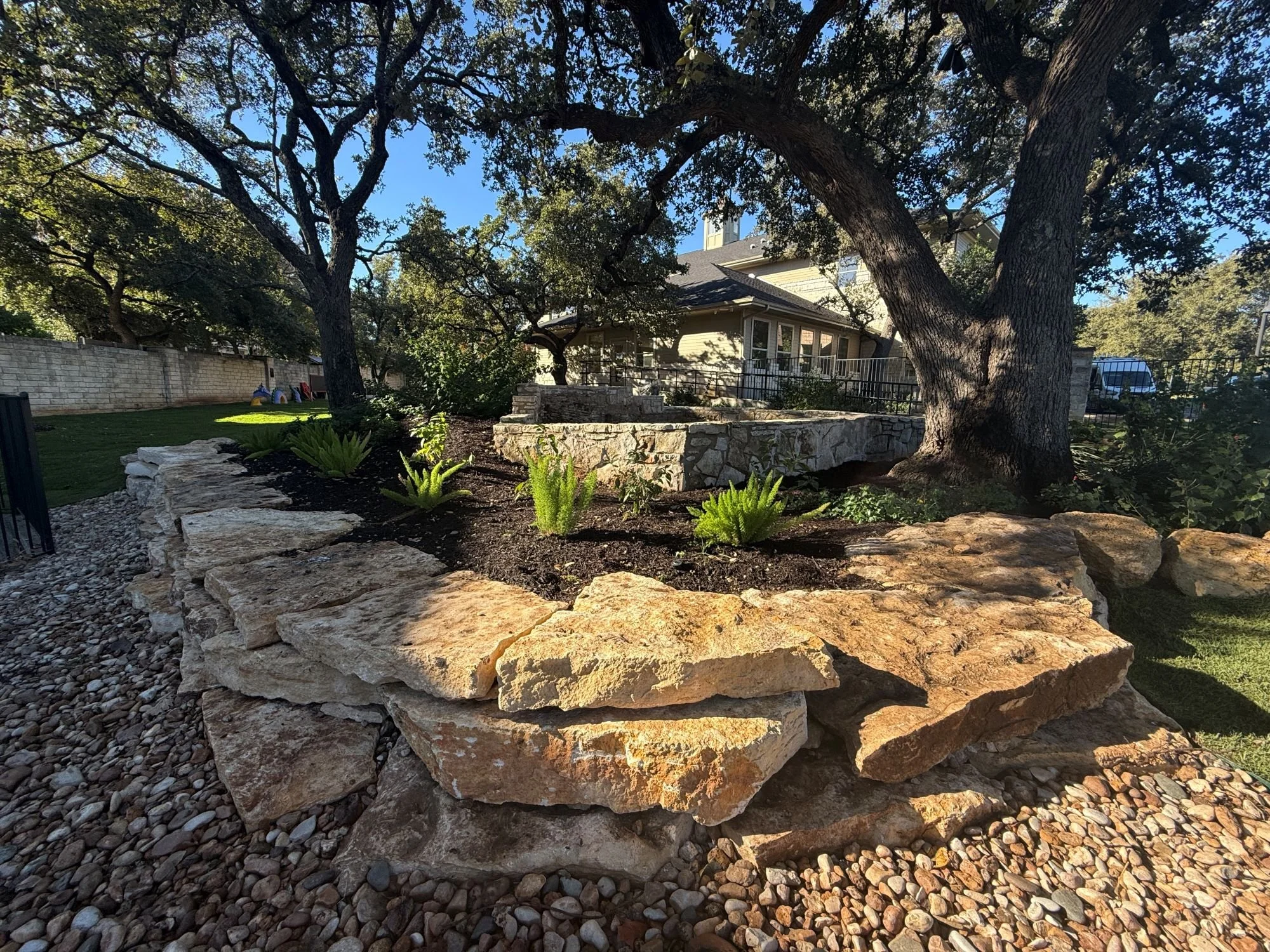 Stone walls at heritage tree with native plantings at westbank community library in austin texas