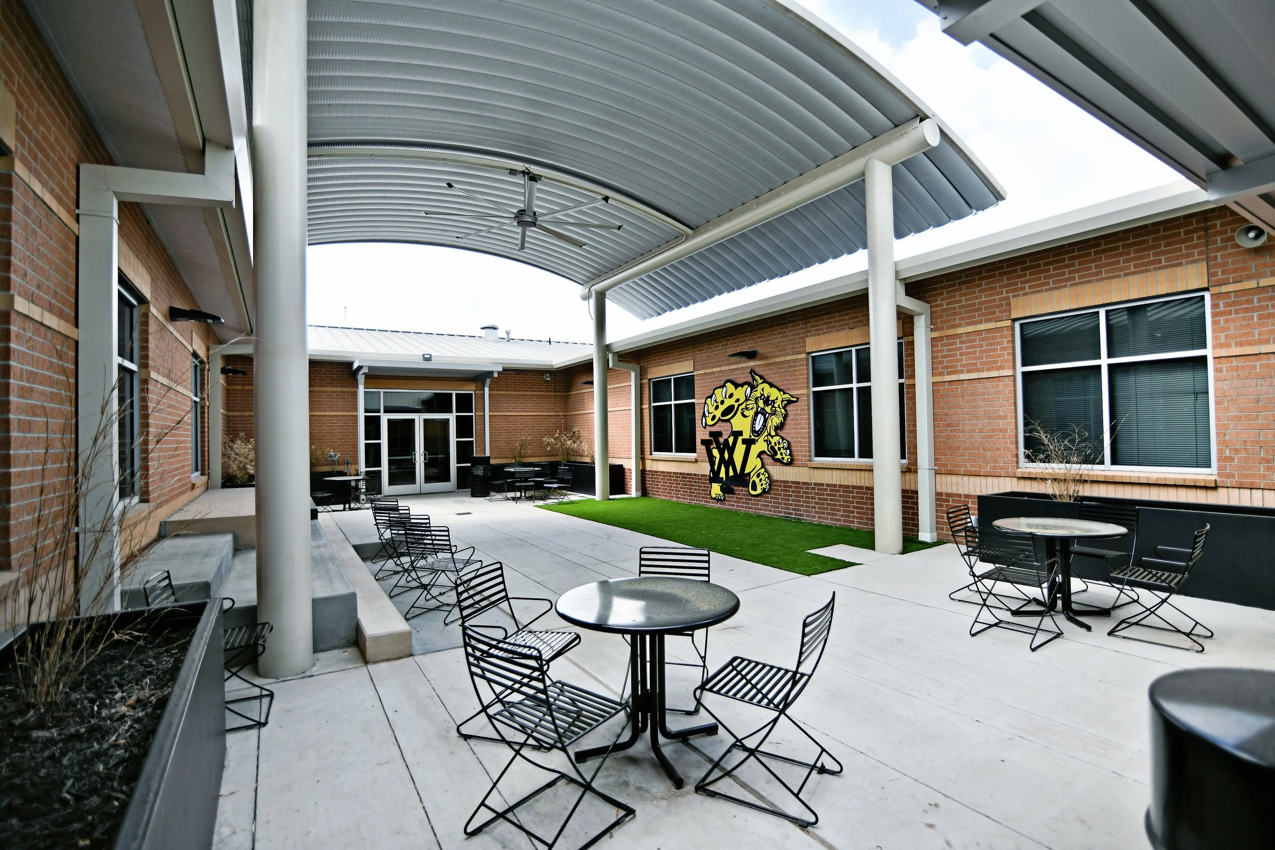 School courtyard space with shade structure and movable seating, terraced seating and artificial turf courtyard features