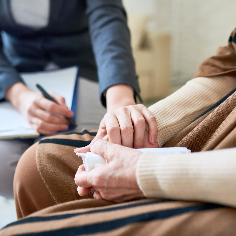 A comforting gesture where one person holds another's hand, both seated. The person on the left is taking notes.
