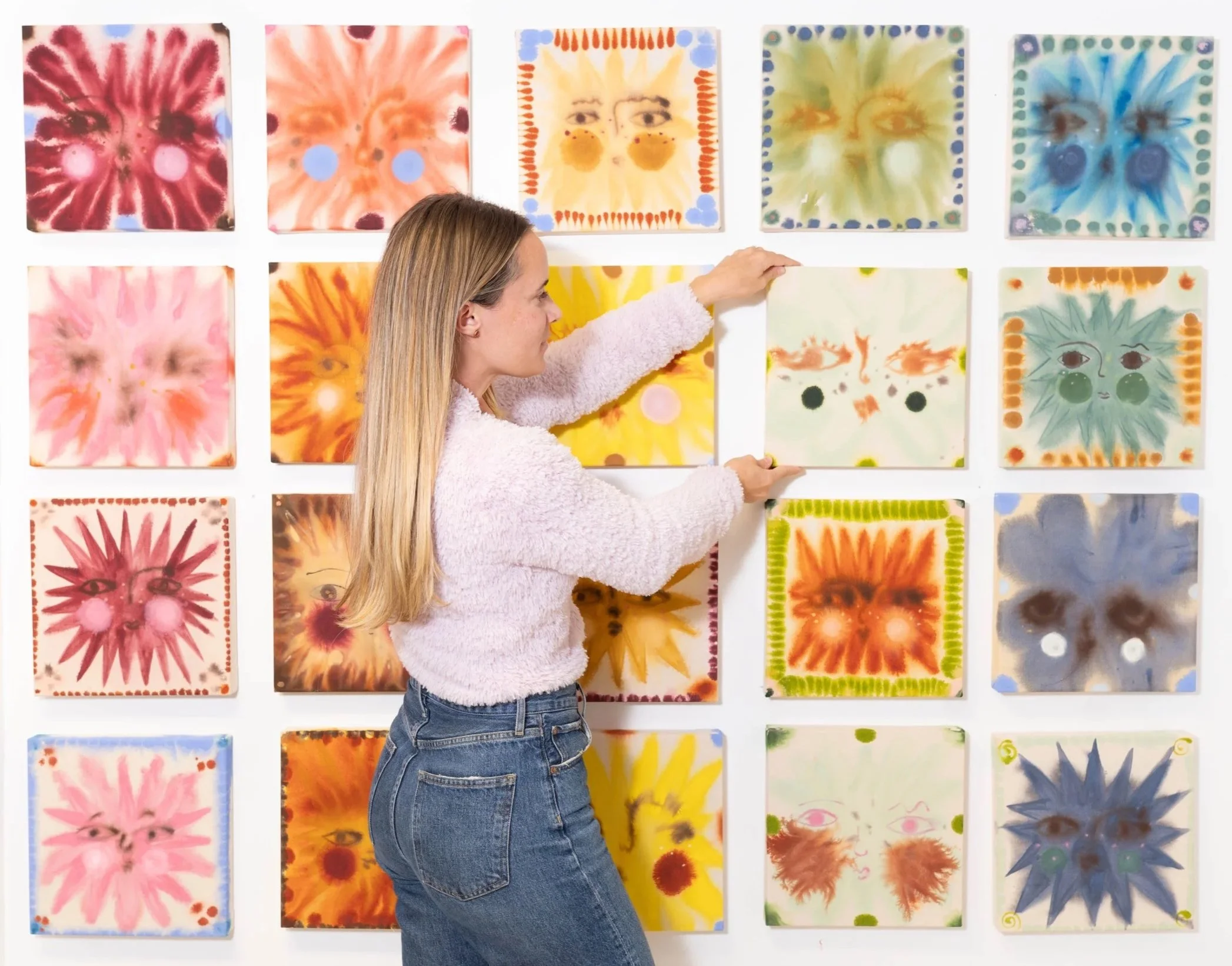 Woman arranging colorful floral artwork on a gallery wall during a commercial photography session in South Carolina, photographed by Chandler Cox