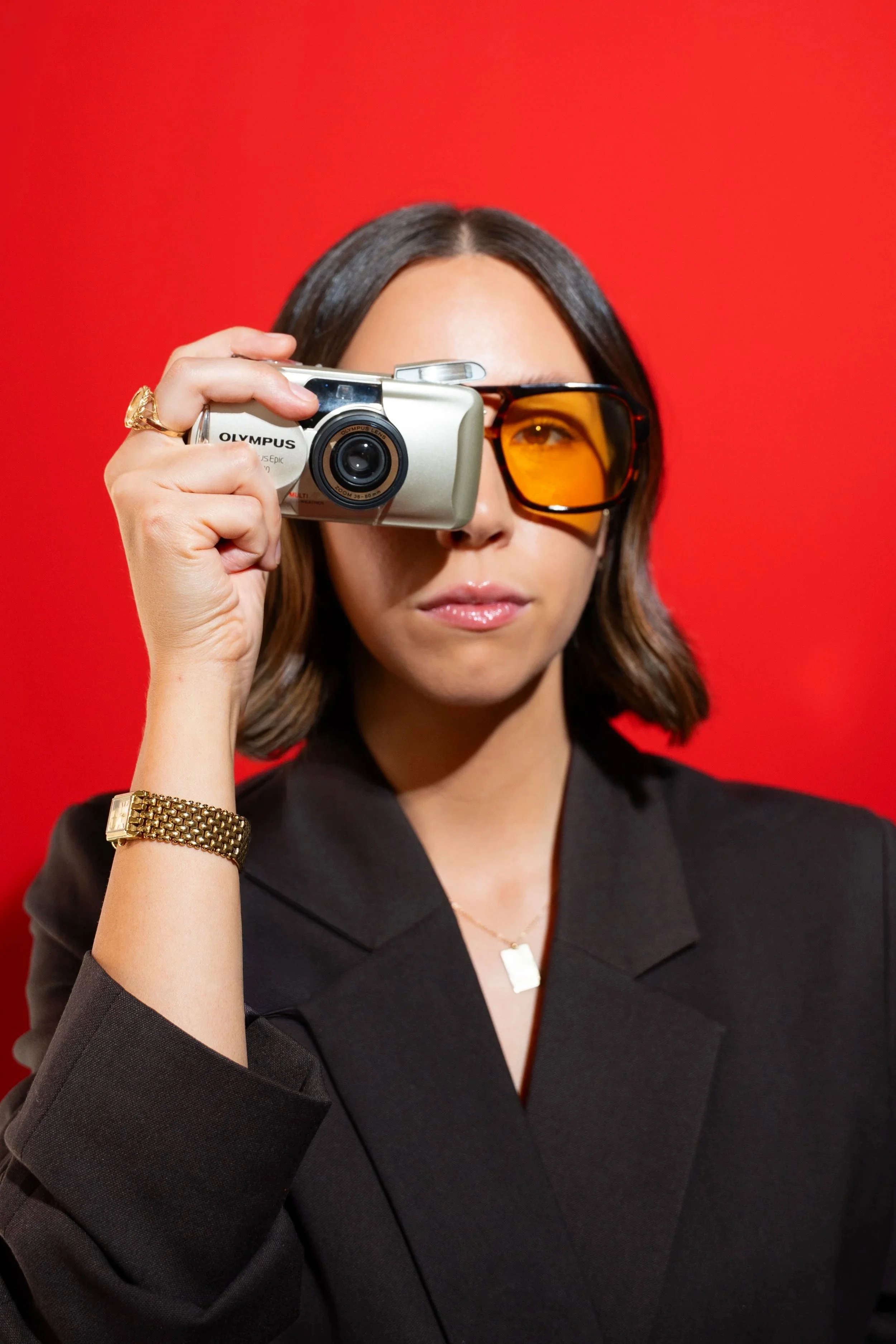 Bold personal branding portrait photography by Chandler Cox — woman in black blazer holding Olympus film camera against red background, Columbia SC editorial portrait photographer