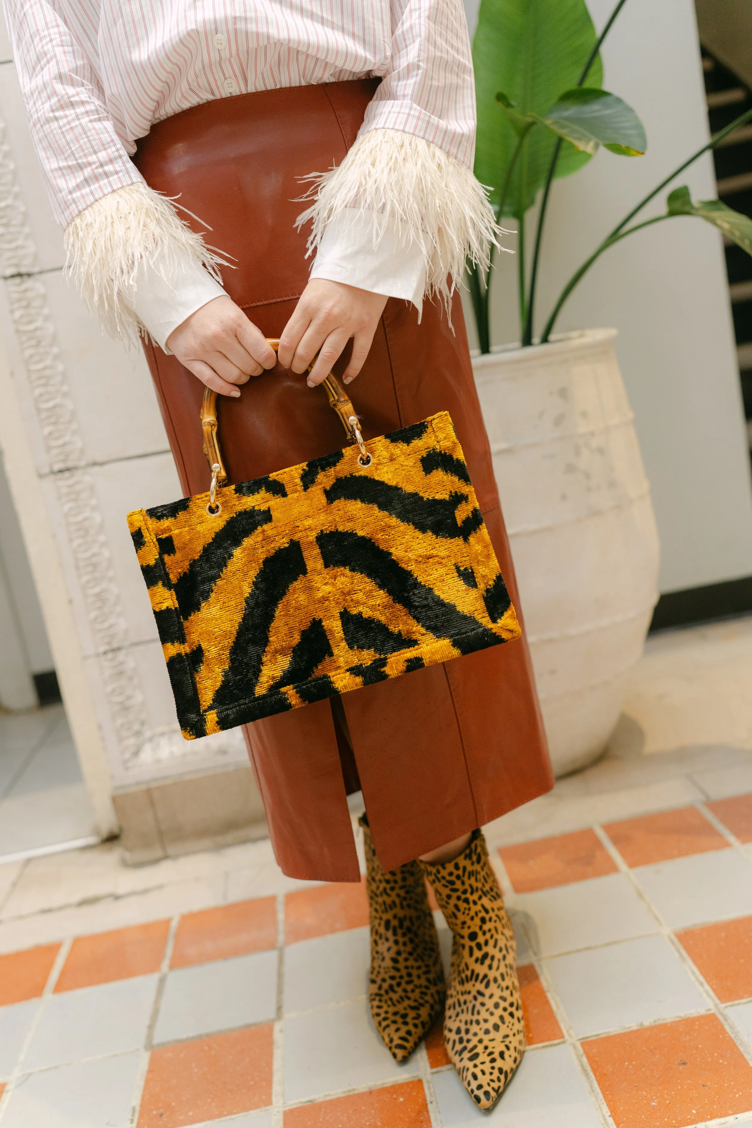 Detail shot of a tiger-print handbag, cognac leather skirt, feather-cuff sleeves, and leopard ankle boots on a tile floor, captured during a boutique product photography session in Columbia, SC