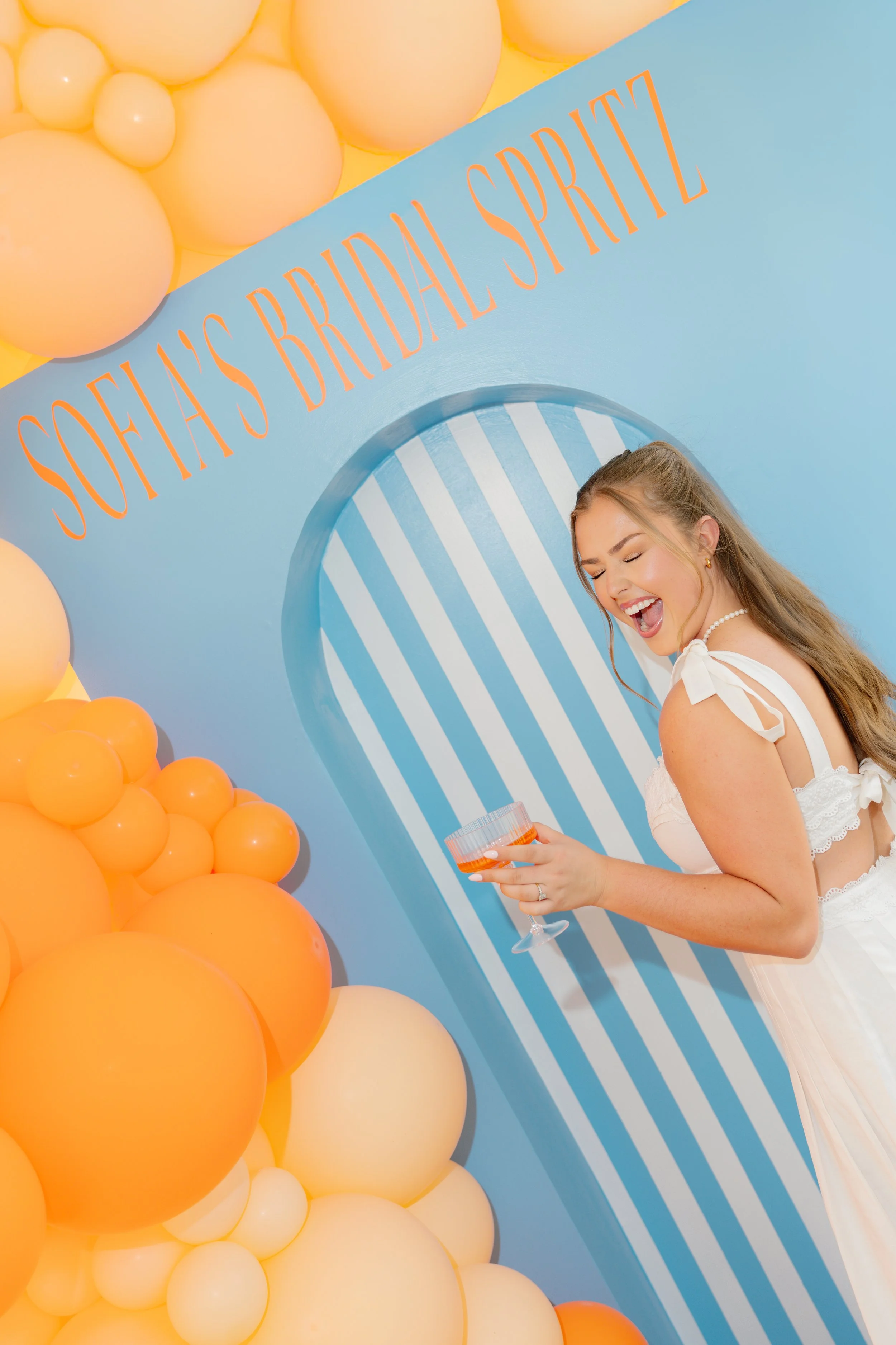 Bridal event and bachelorette party photography by Chandler Cox — bride laughing in front of custom branded balloon arch backdrop, Columbia SC wedding and event photographer