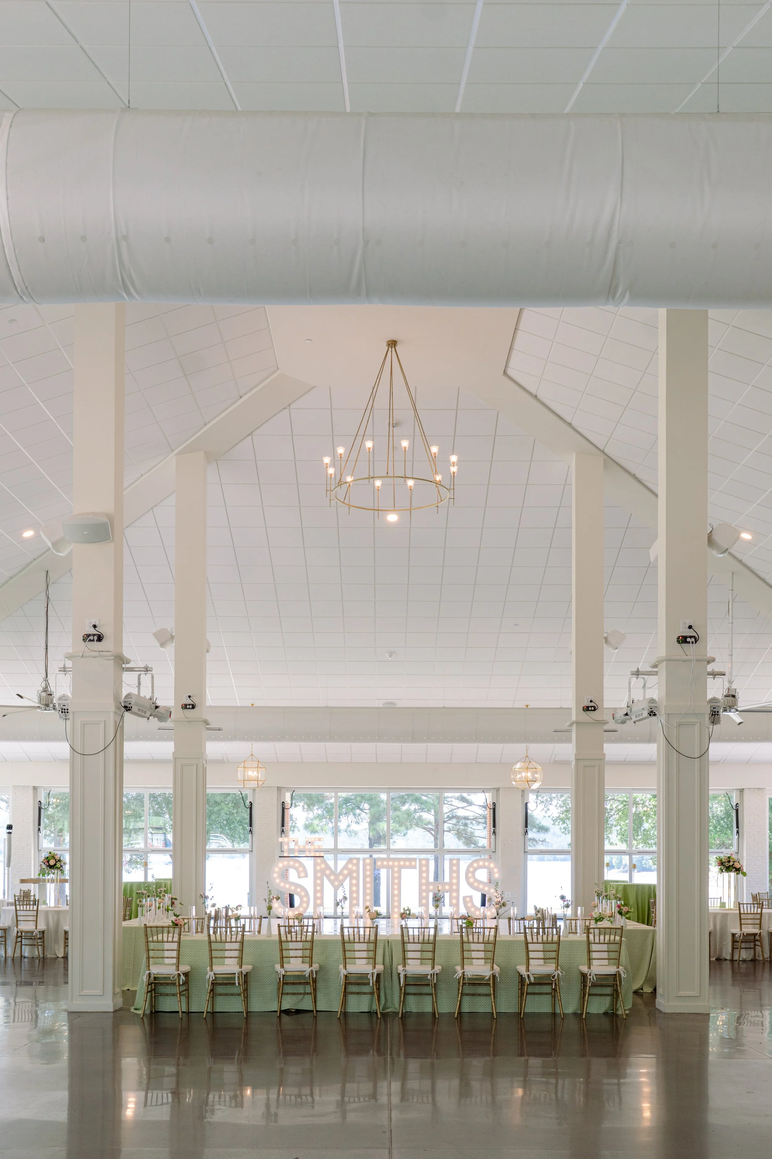 Elegant white barn wedding reception venue with chandelier and sage green chairs, Clemson SC wedding photographer