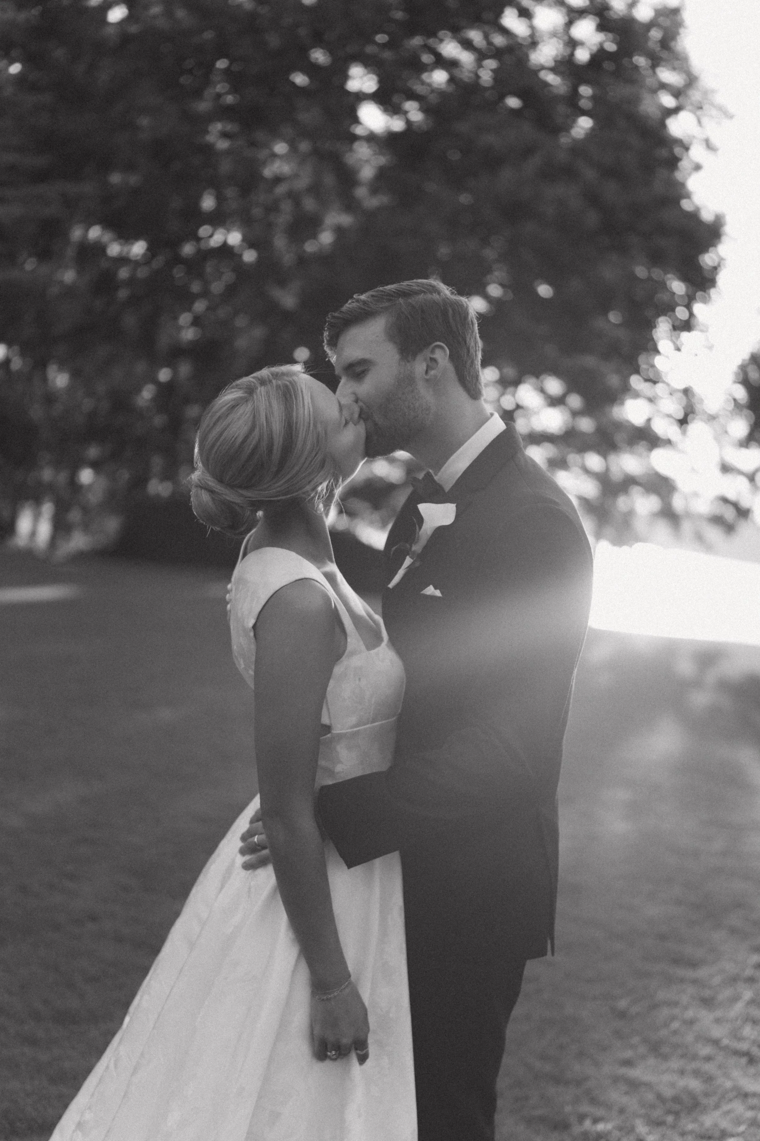 Black and white photo of bride and groom sharing kiss with warm backlit sunset glow, South Carolina wedding photographer