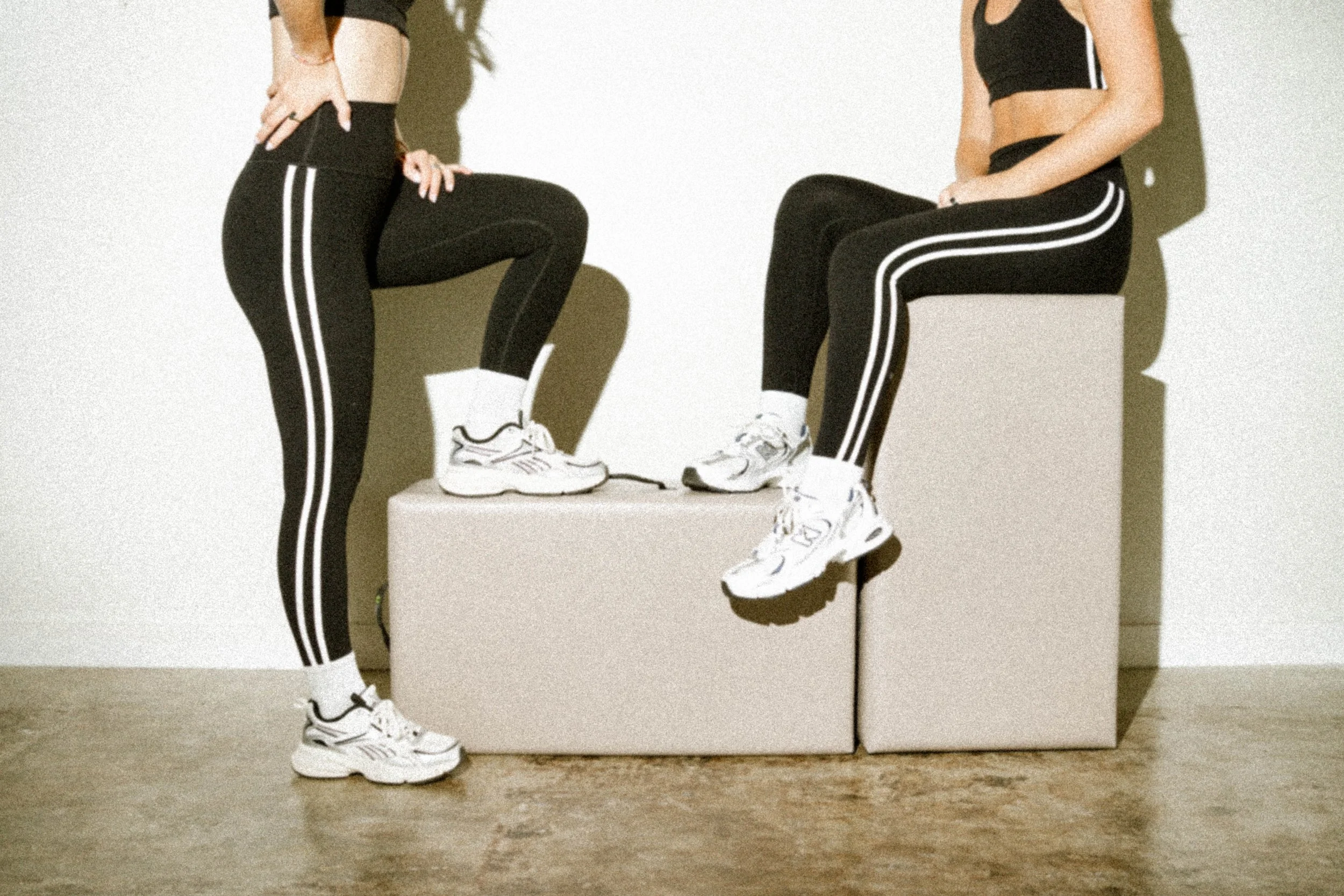 Two models in black activewear posed on minimalist blocks against a white background — commercial apparel photography by Chandler Cox, Columbia, SC