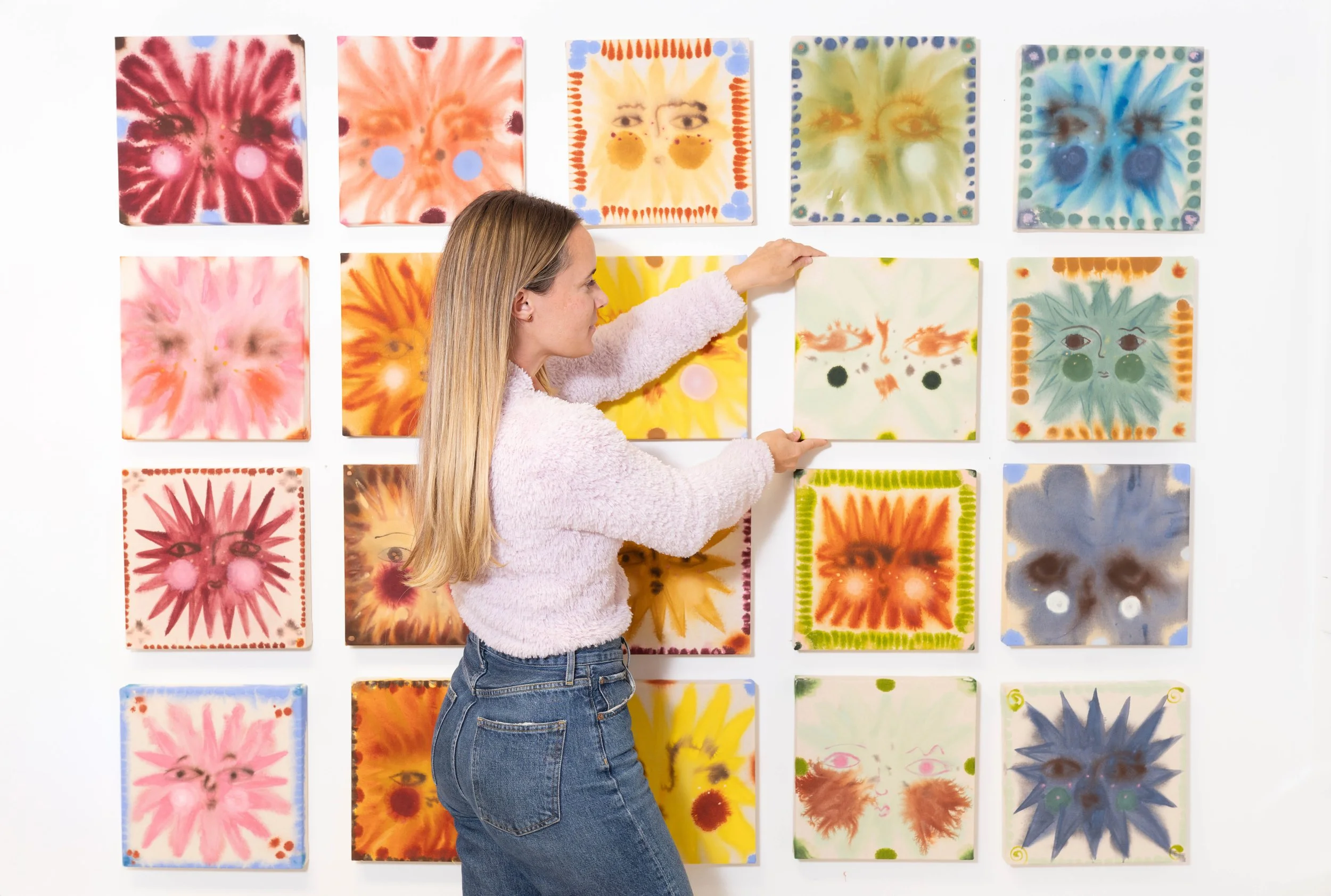 Woman arranging colorful abstract floral art prints on a white gallery wall — commercial photography by Chandler Cox, Columbia, SC