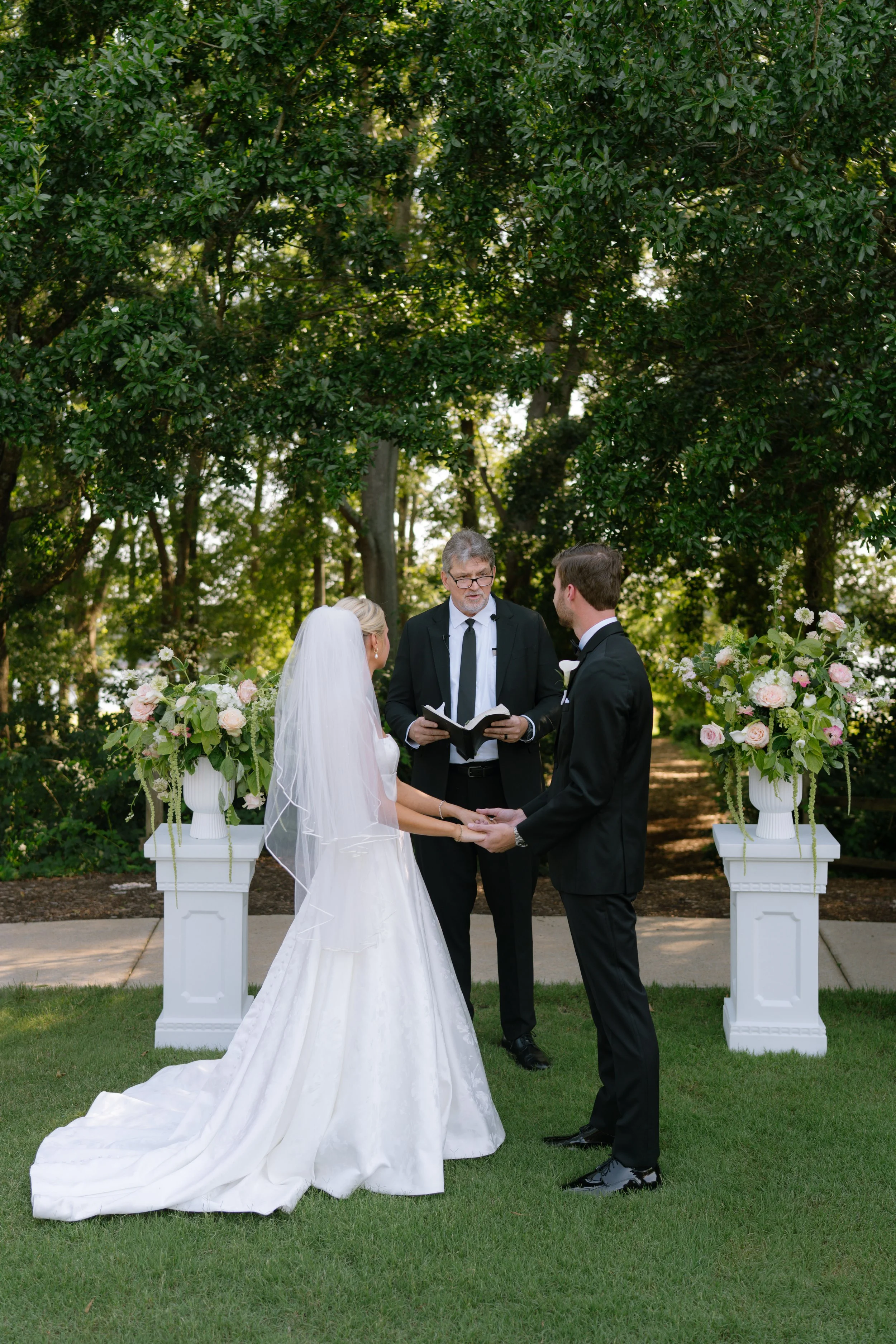 Bride and groom holding hands during outdoor ceremony with white floral pedestal arrangements, South Carolina wedding photographer