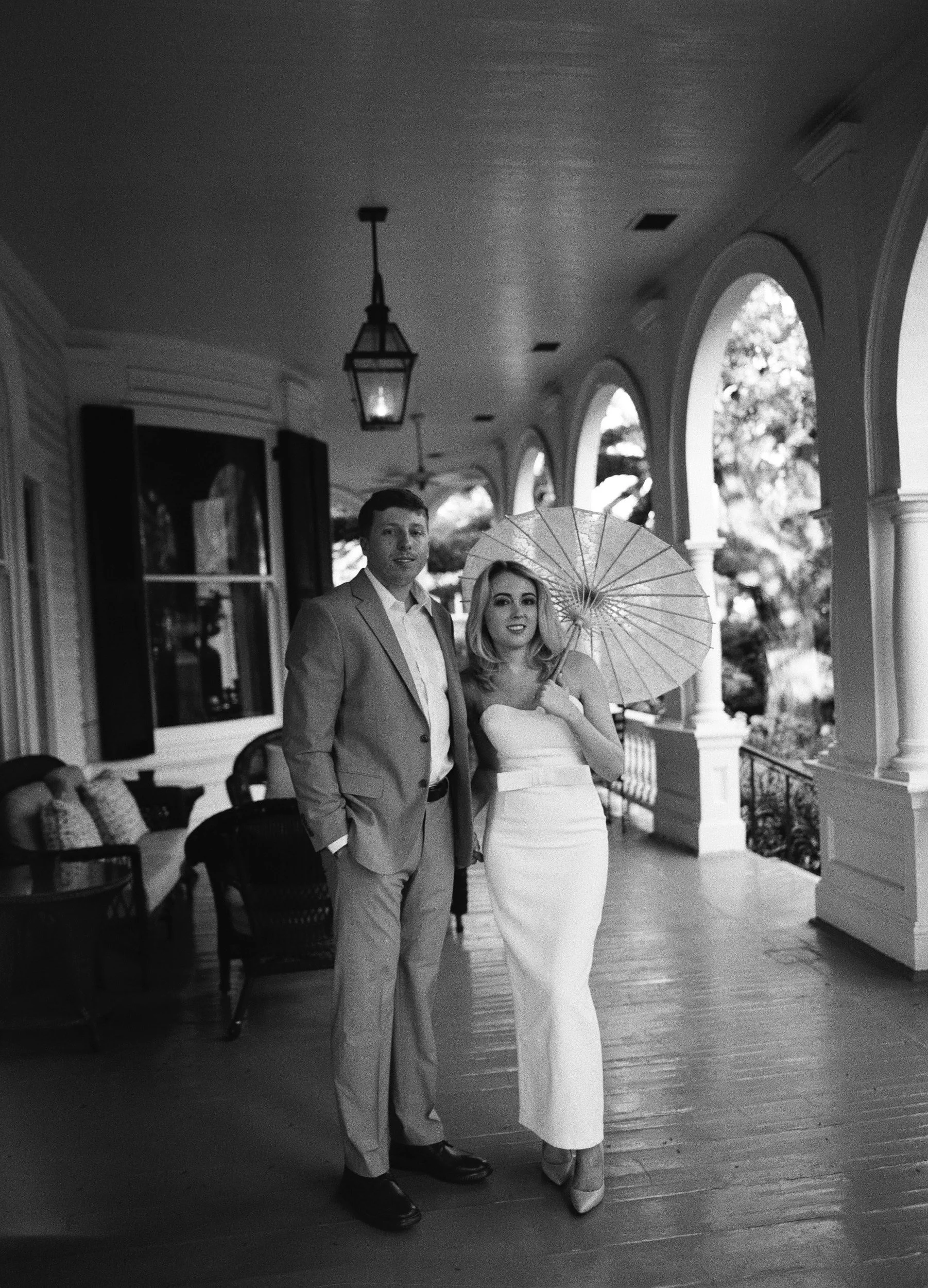 Bride and groom posing on a historic southern venue porch with a parasol, shot on black and white film by Columbia SC wedding photographer Chandler Cox