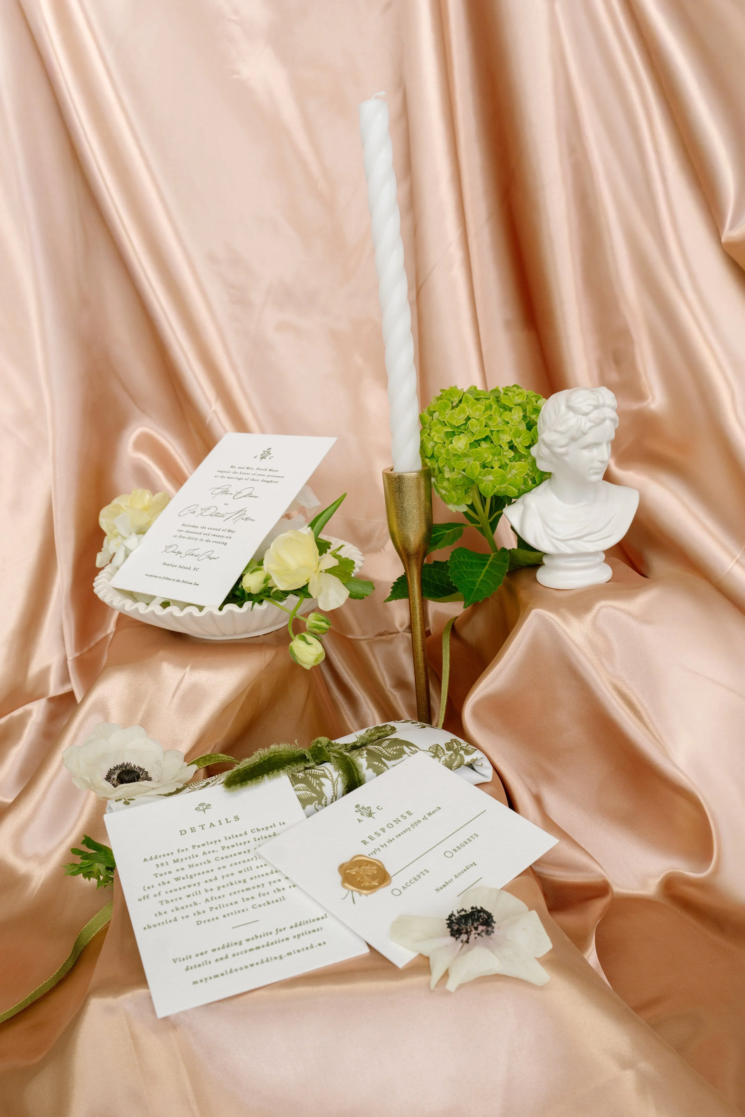 Wedding invitation flat lay with gold wax seal, taper candle, and green hydrangea on champagne silk, Charleston SC wedding photographer