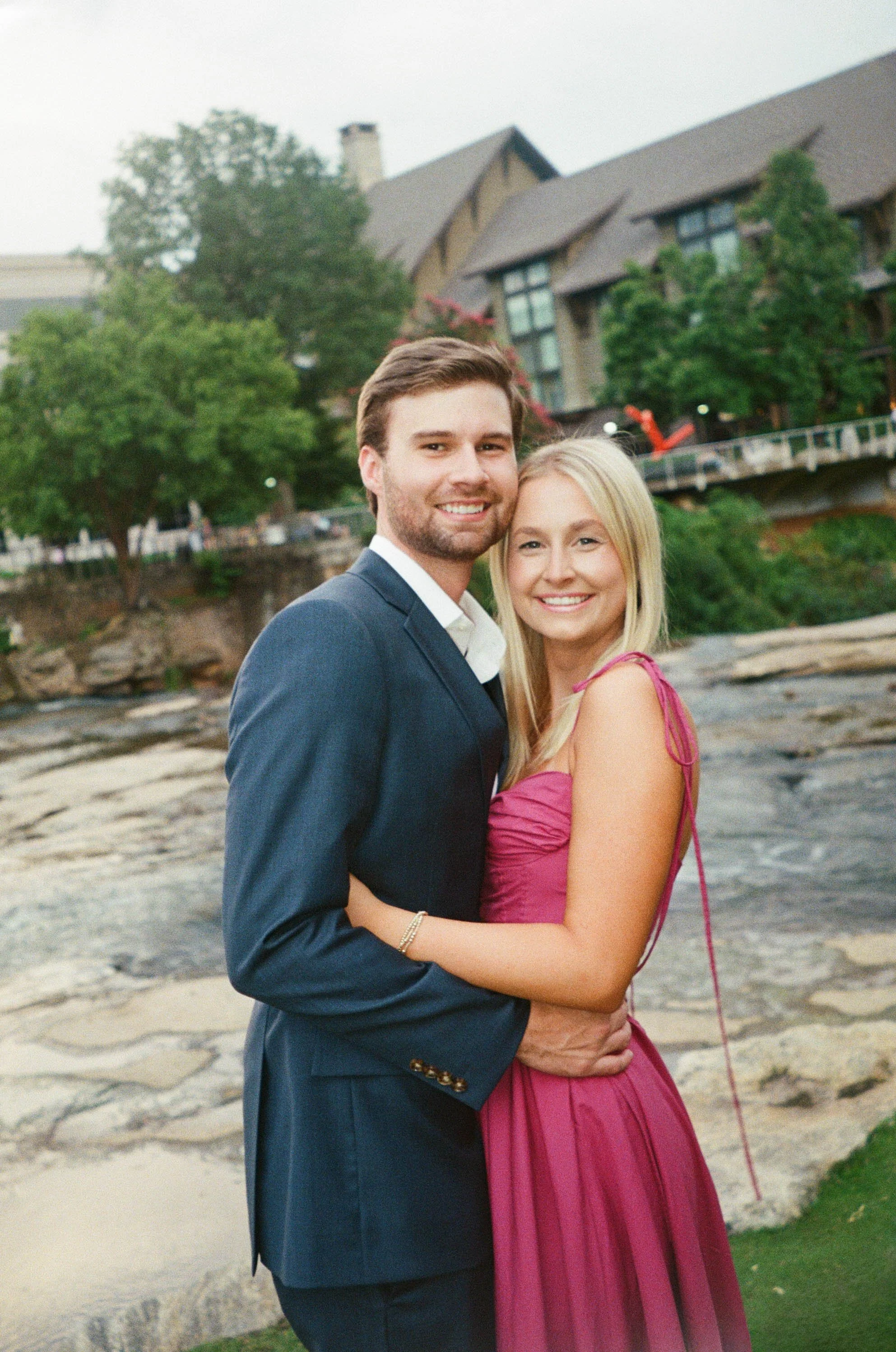 Film engagement session photography by Chandler Cox — couple embracing and smiling by rocky riverfront at Falls Park Greenville SC, South Carolina engagement and wedding photographer