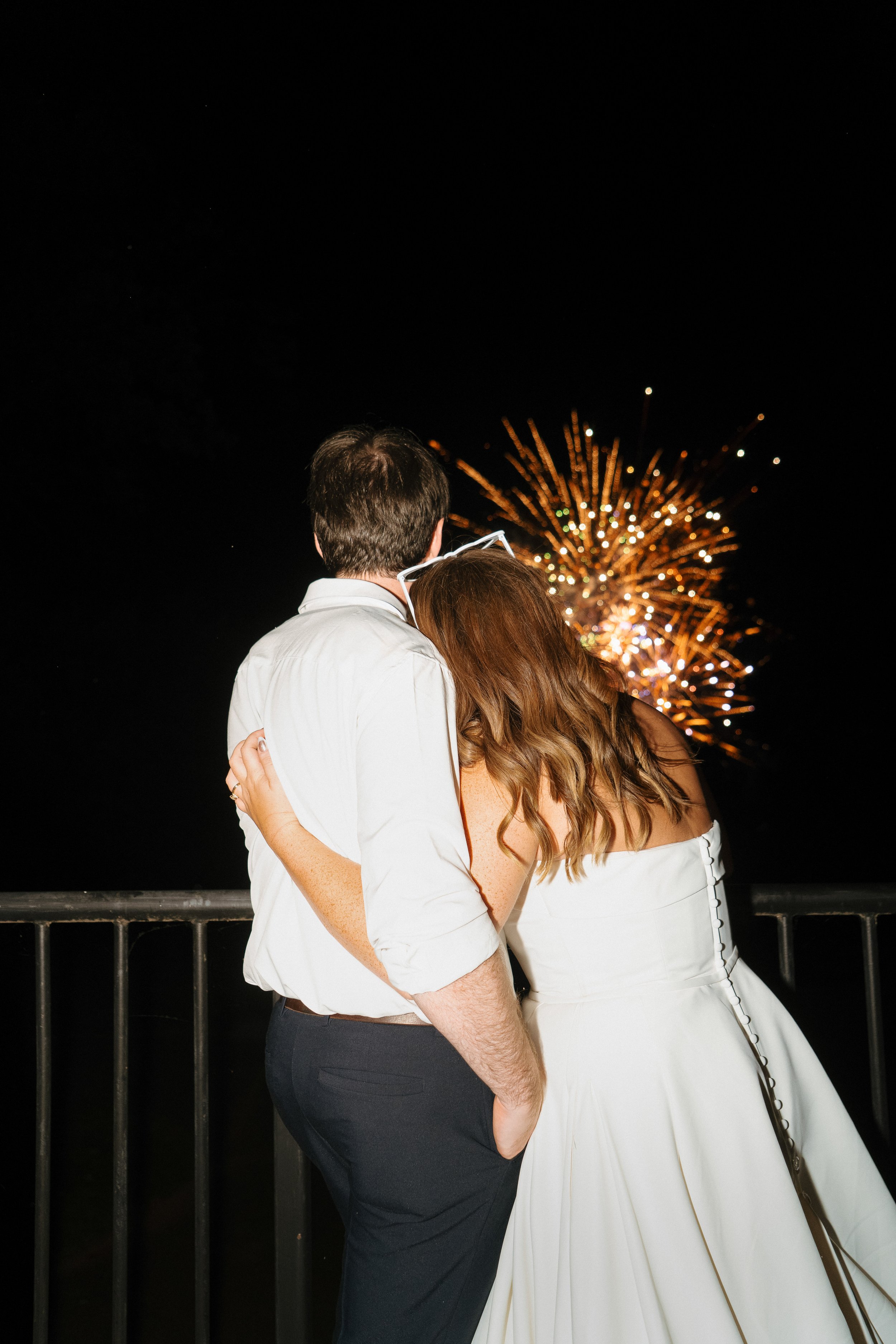 A couple embracing at night with firework display in the background.