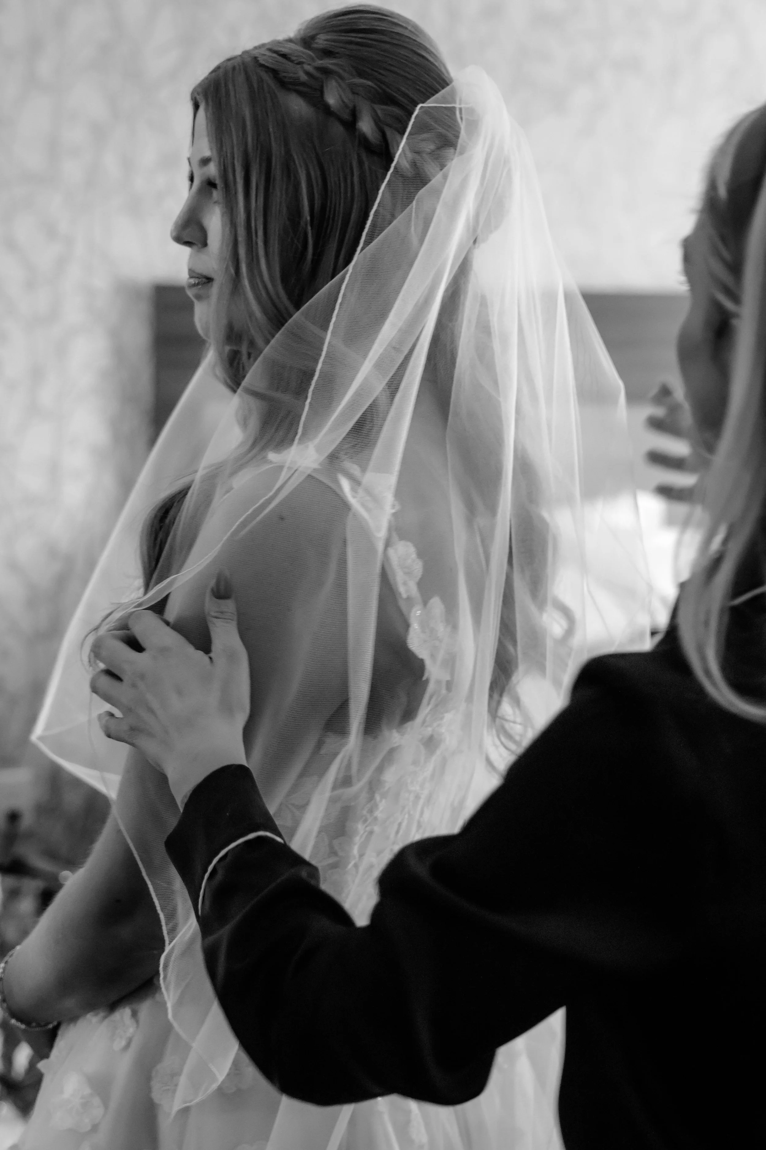 A bride with long hair wearing a veil on her head, standing with her eyes closed, as someone tenderly touches her shoulder in Chicago, IL.