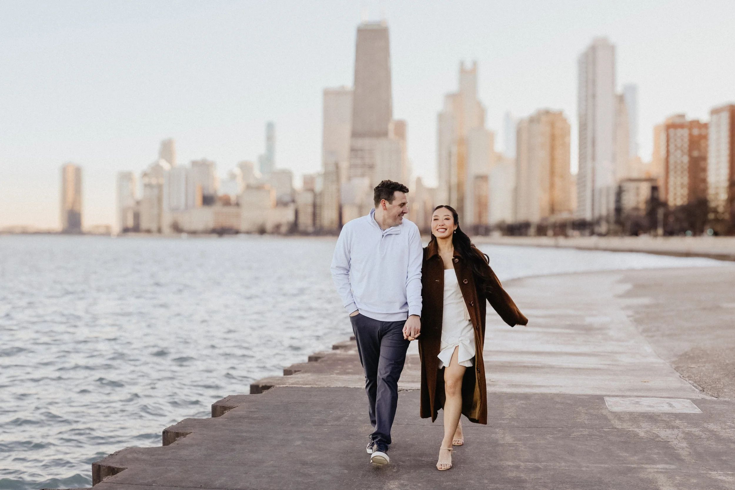 A couple walks together on the breakwater near the lakefront in Chicago with the skyline in the background.