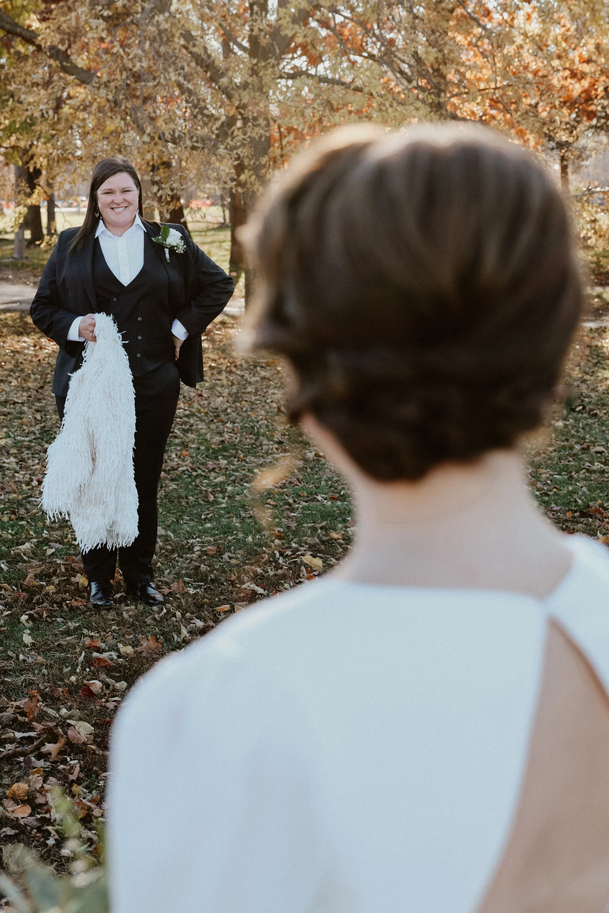 A bride looks toward her wife across a field of fall foliage in Chicago.