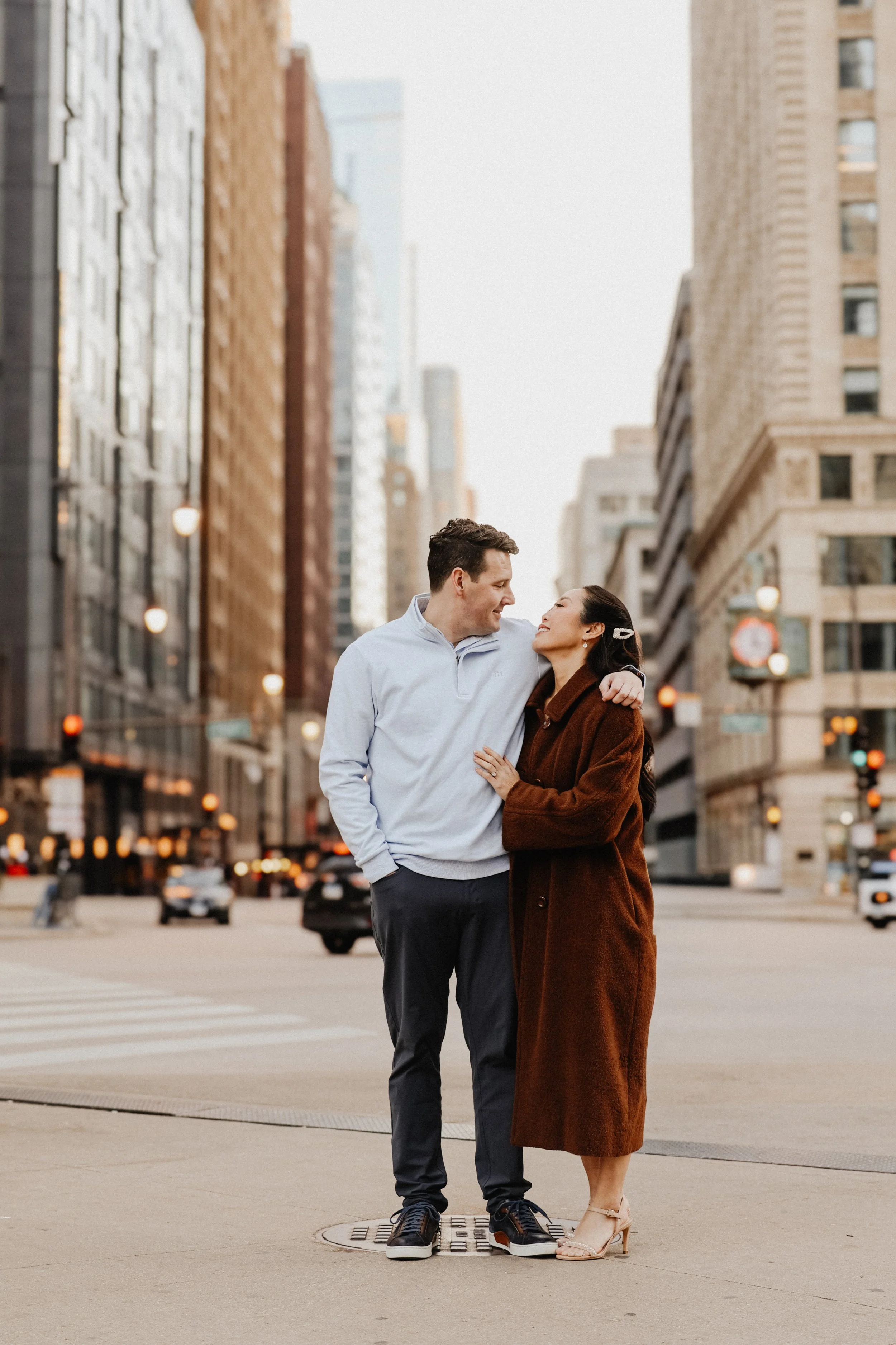 Two people pose for engagement photos in downtown Chicago with high-rises in the background.