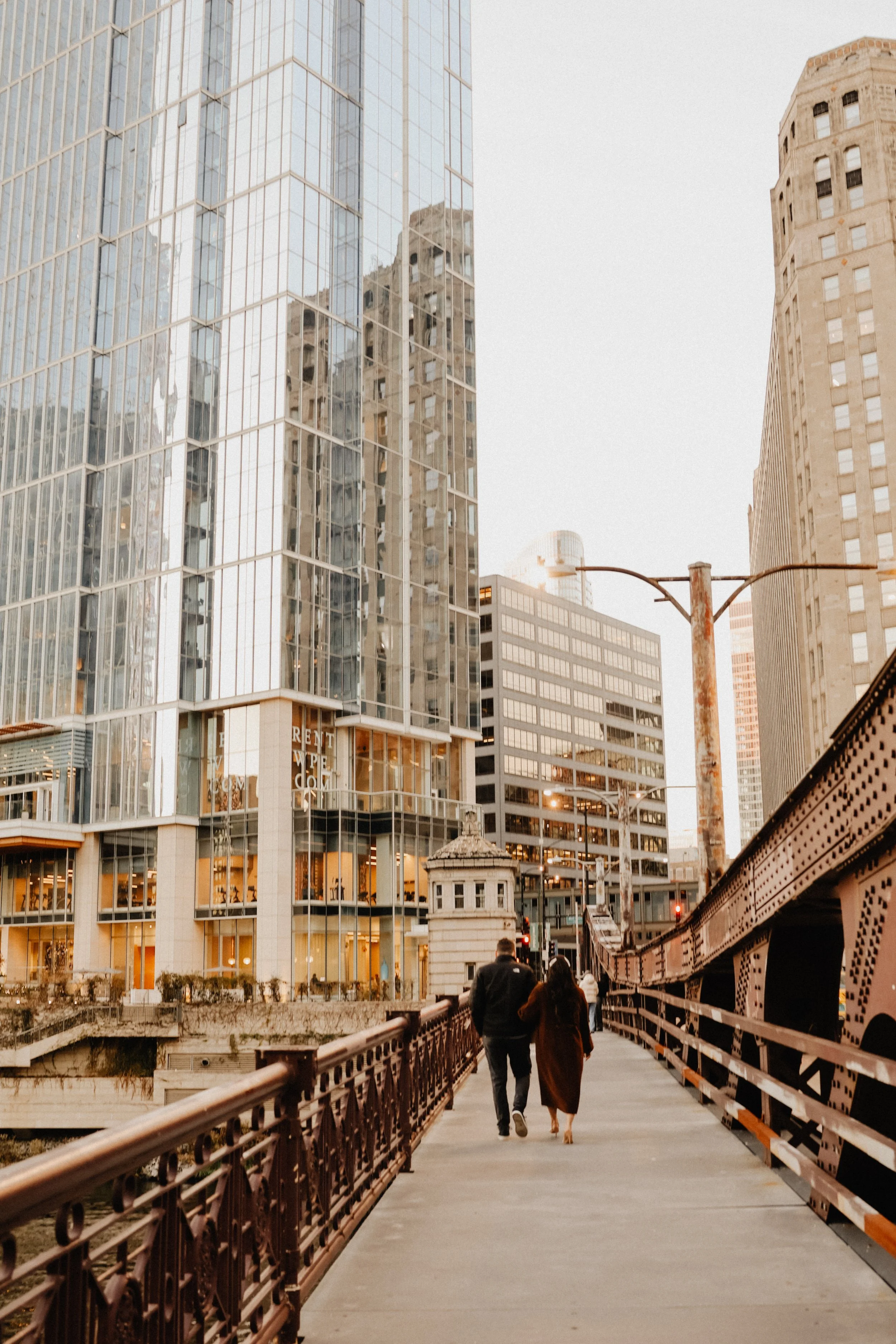 Two people walk toward an apartment building in River North Chicago along a bridge walkway with skyline in the background.