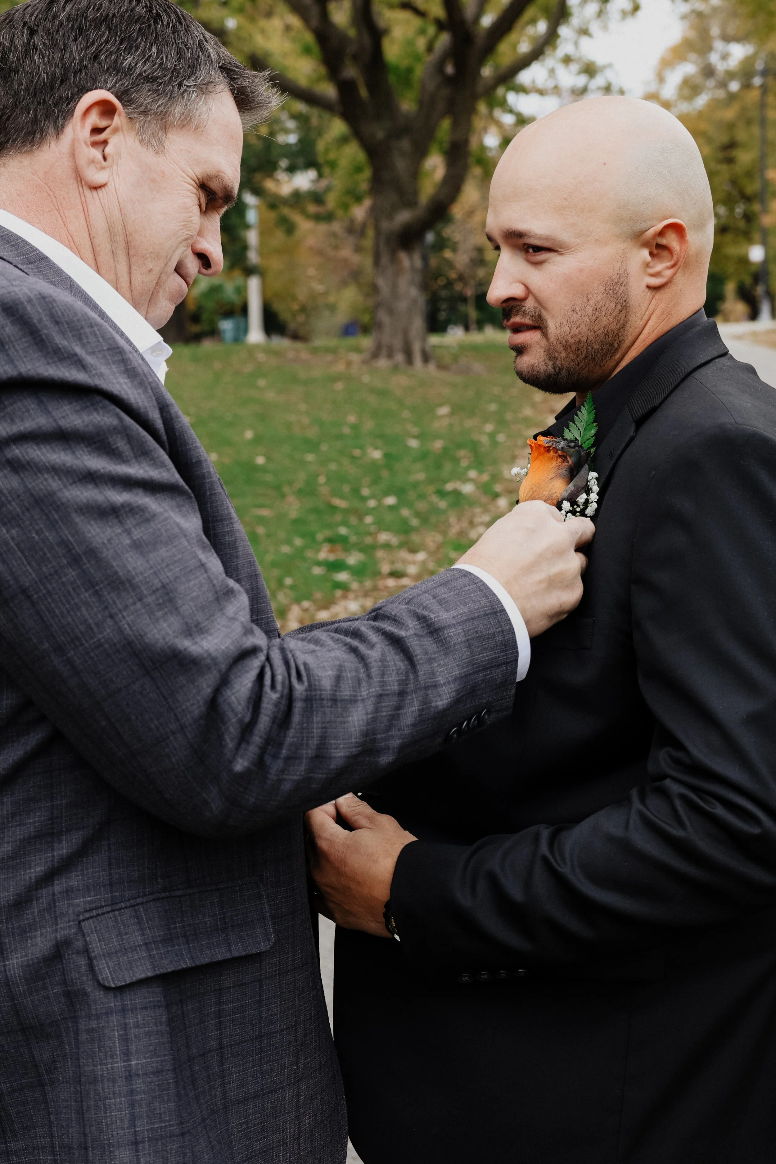 A groom's father pins his floral onto his jacket in Lincoln Park, Chicago, IL.