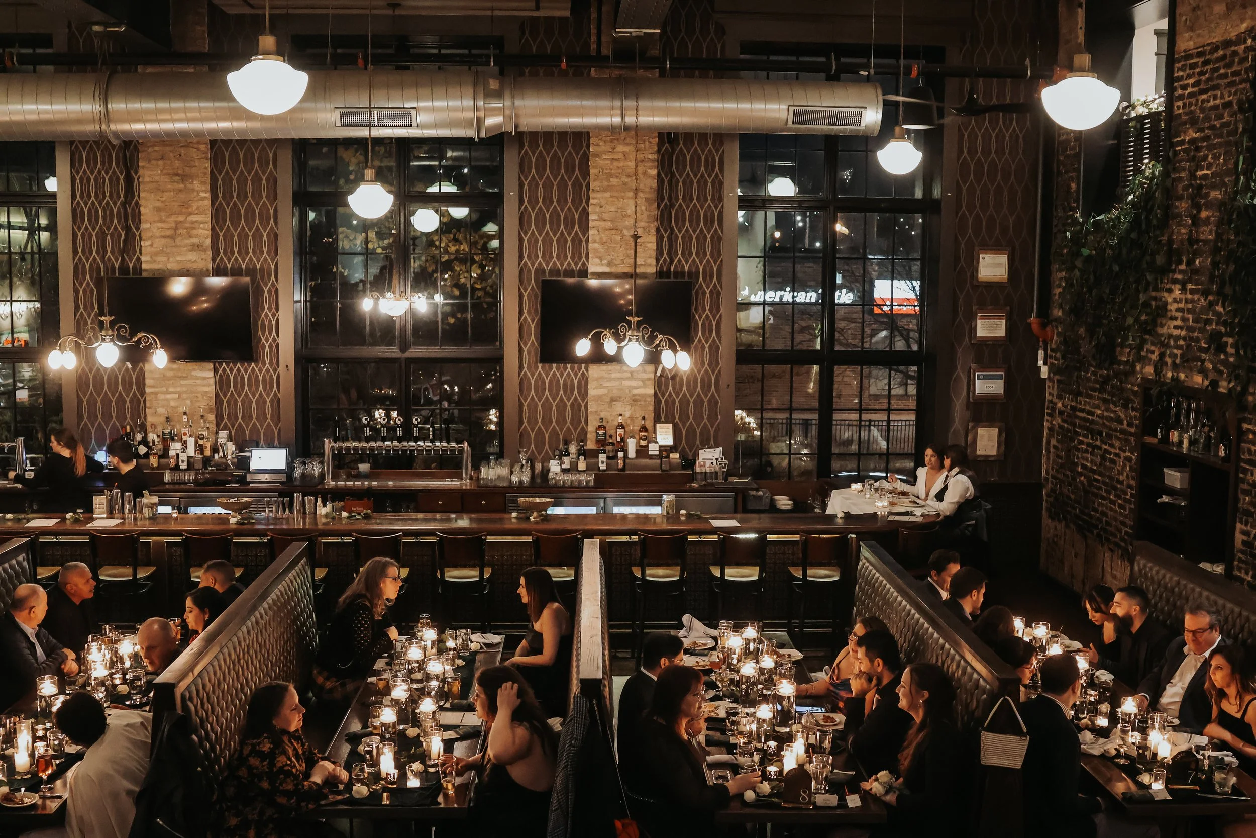 A wide view of friends and family celebrating a wedding in the Eris Brewery and Cider House with a 20s theme and dark wintery decor.