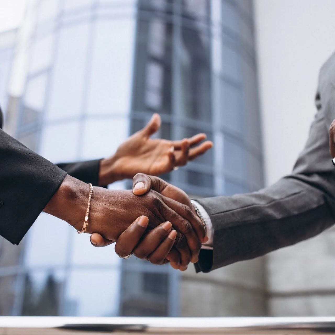 Two people shaking hands in a business setting with a modern office building in the background.