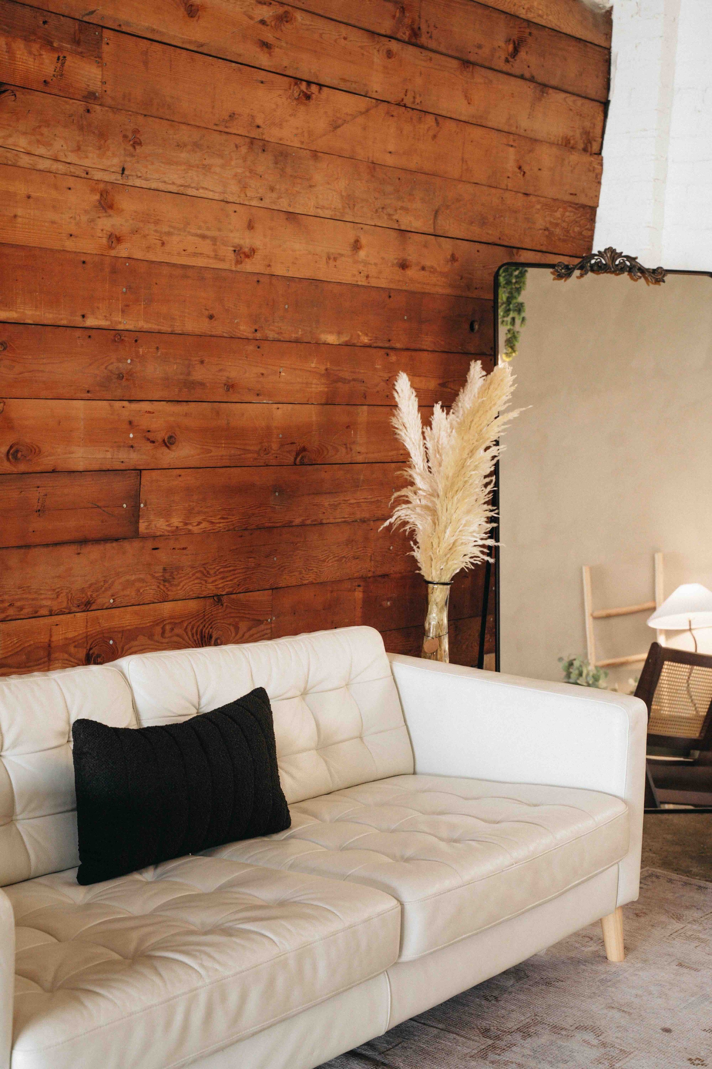 Living room with a white sofa, wooden wall, coffee table with decorative items, and a mirror in the background.