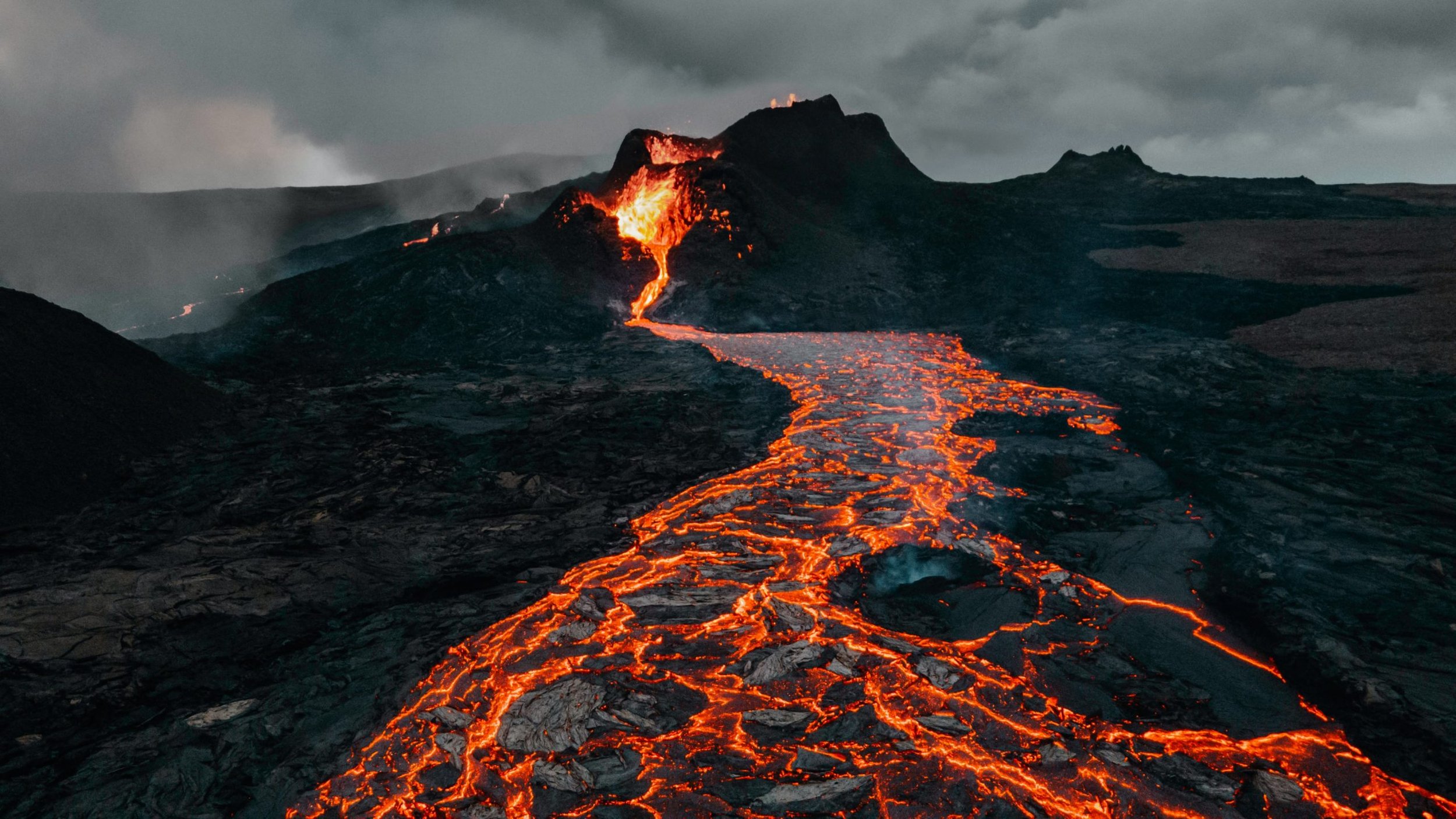Erupting volcano with flowing lava and dark clouds in the sky.