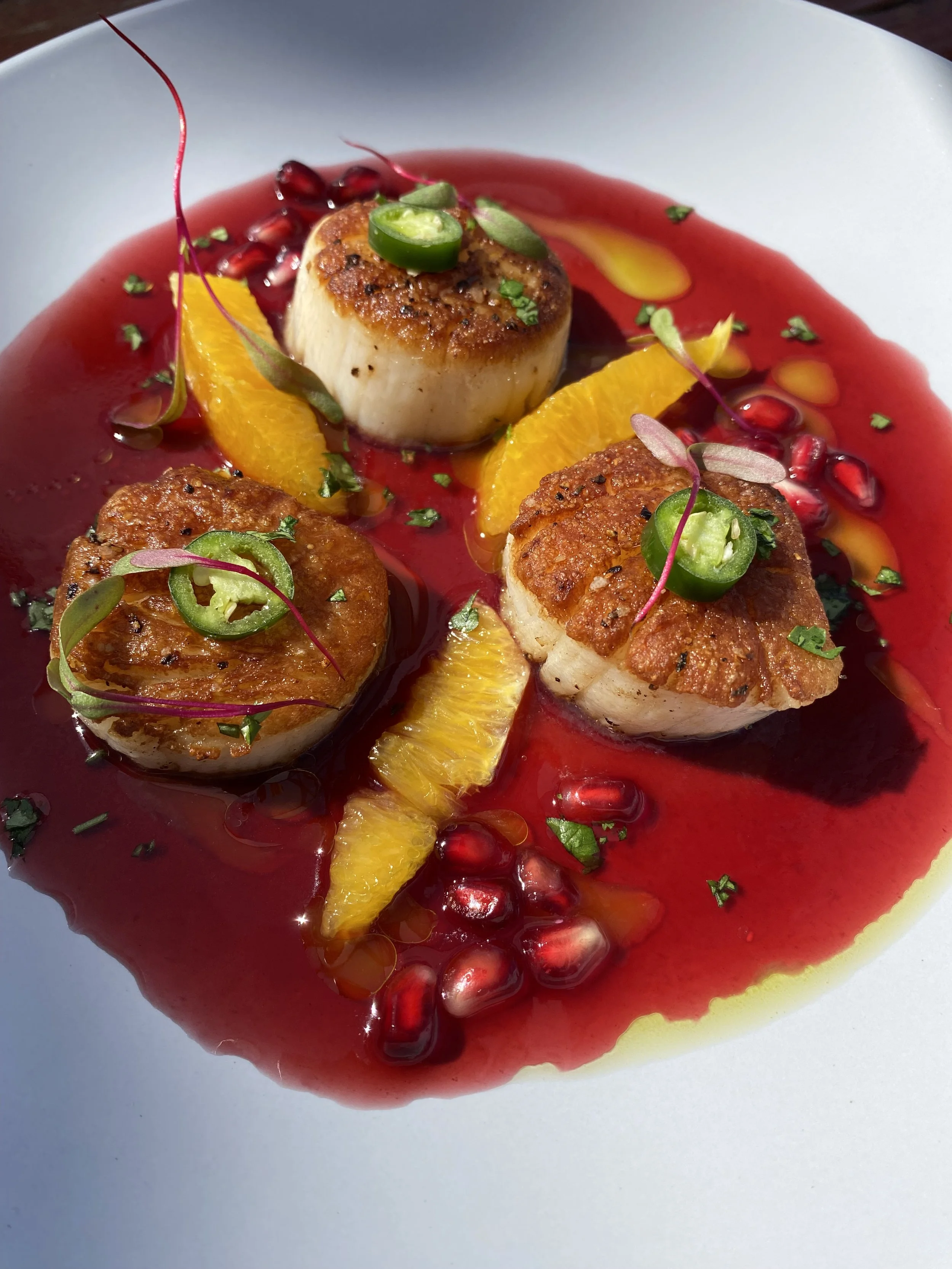 Seared scallops with seasonal vegetables and a vibrant red sauce.