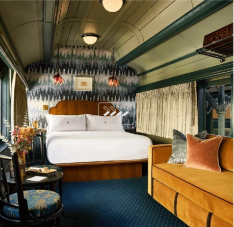 Cozy vintage train car bedroom with a bed, side table, armchair, and sofa, decorated with floral and nature-themed wallpaper, and large windows with curtains and sustainable solution dyed nylon.