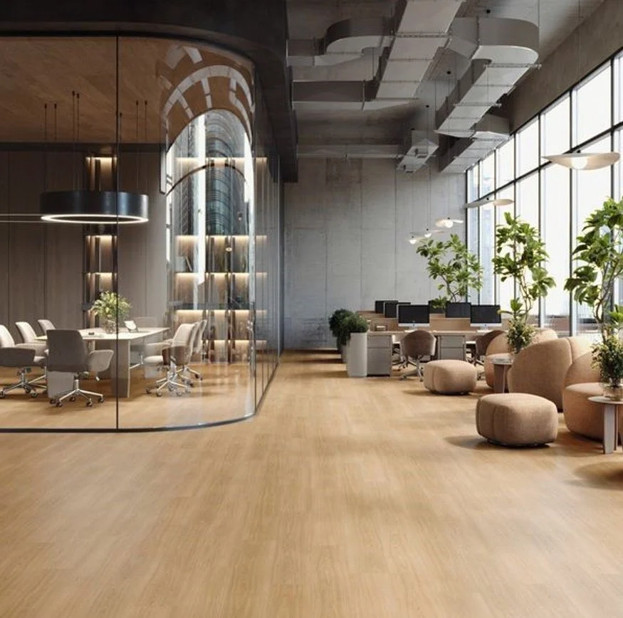Modern office space with glass-walled conference room, light wood flooring, large windows, and comfortable seating with plants and pvc free resilient flooring.